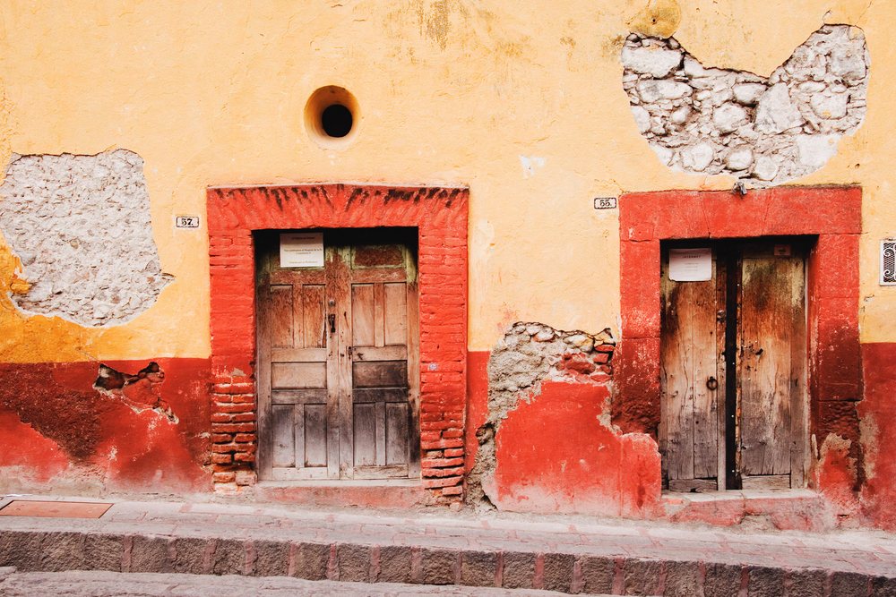 Two weathered wooden doors on yellow and red wall mexico