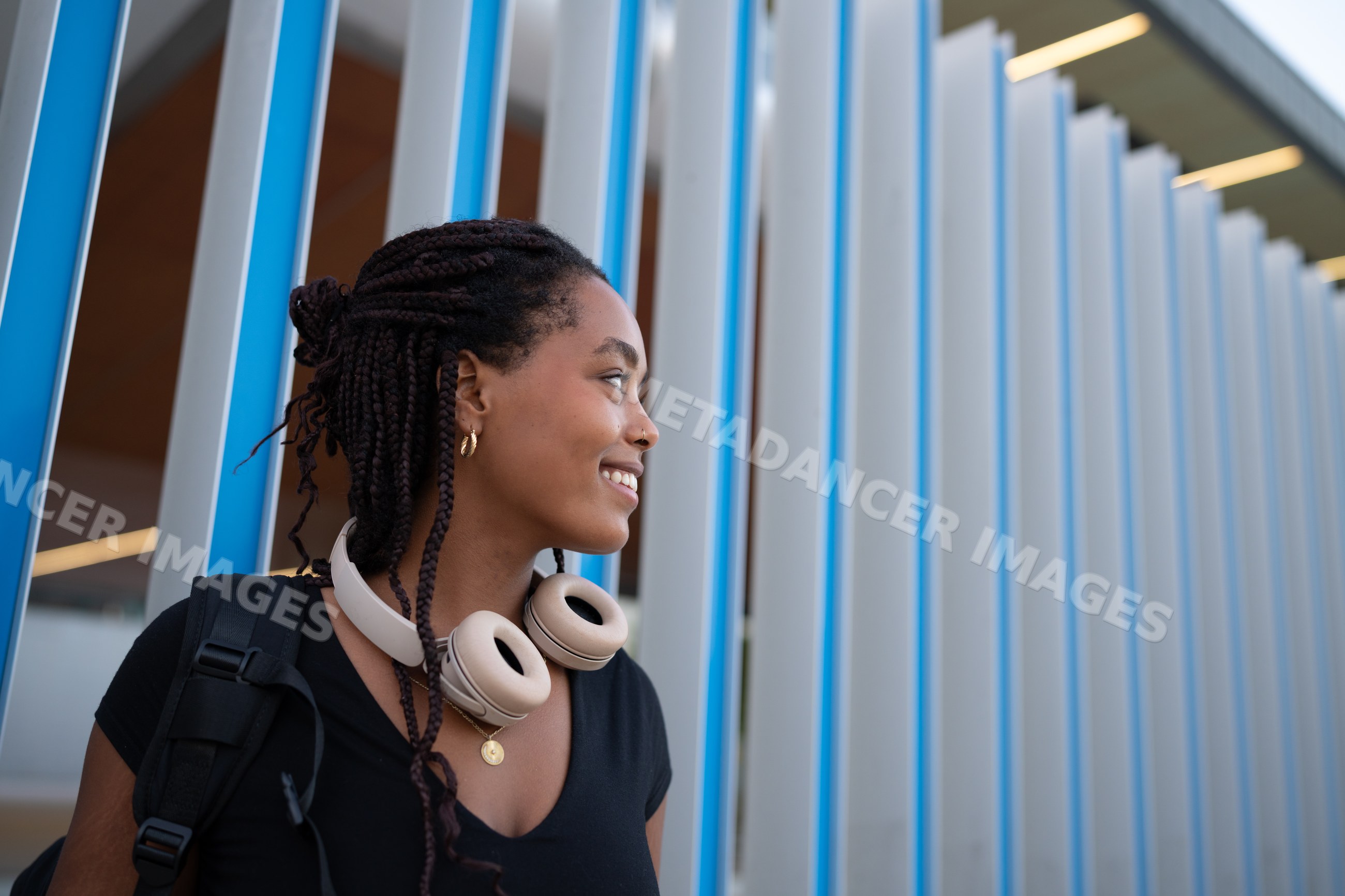 A young African American woman with headphones smiles outdoors