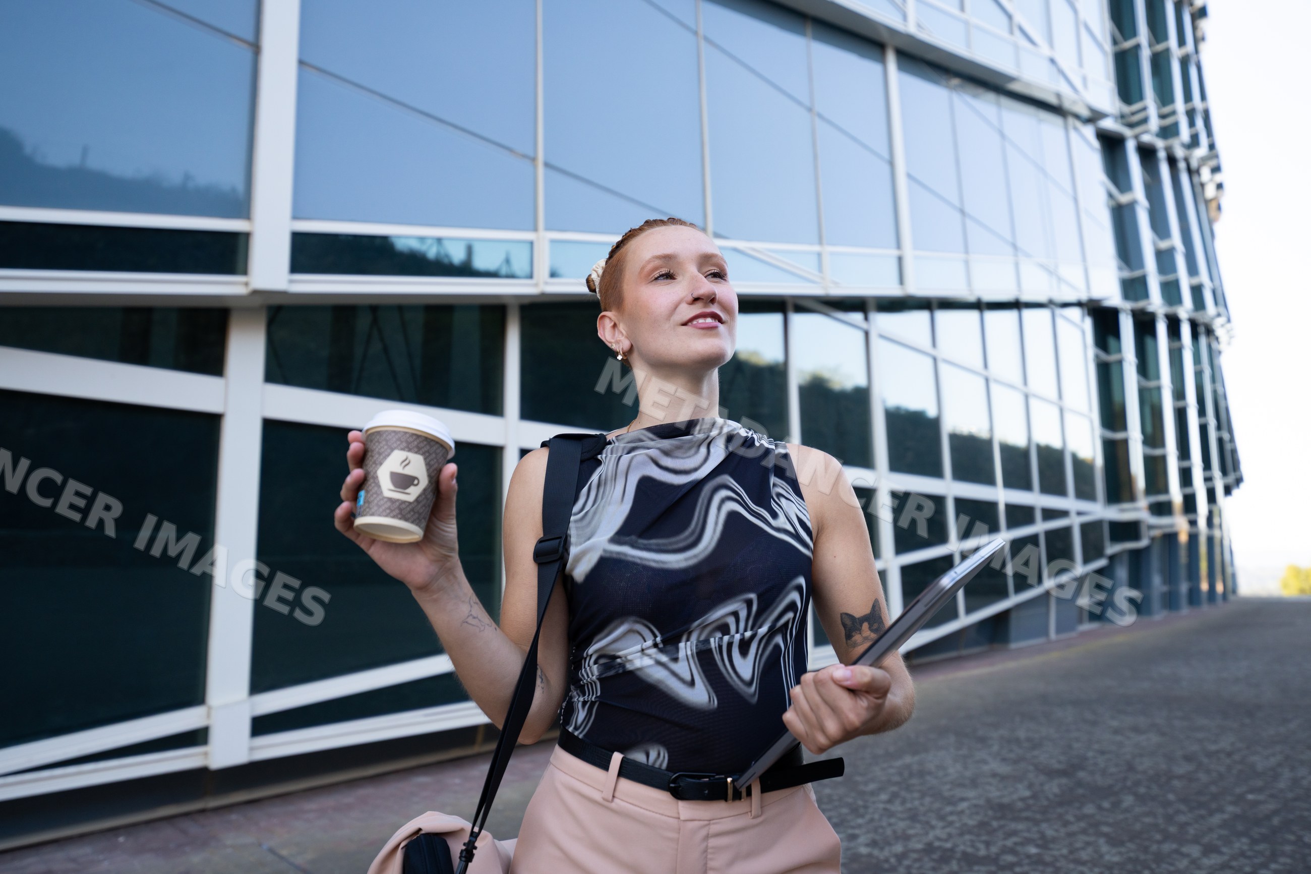 Businesswoman holding coffee cup and laptop outside modern office