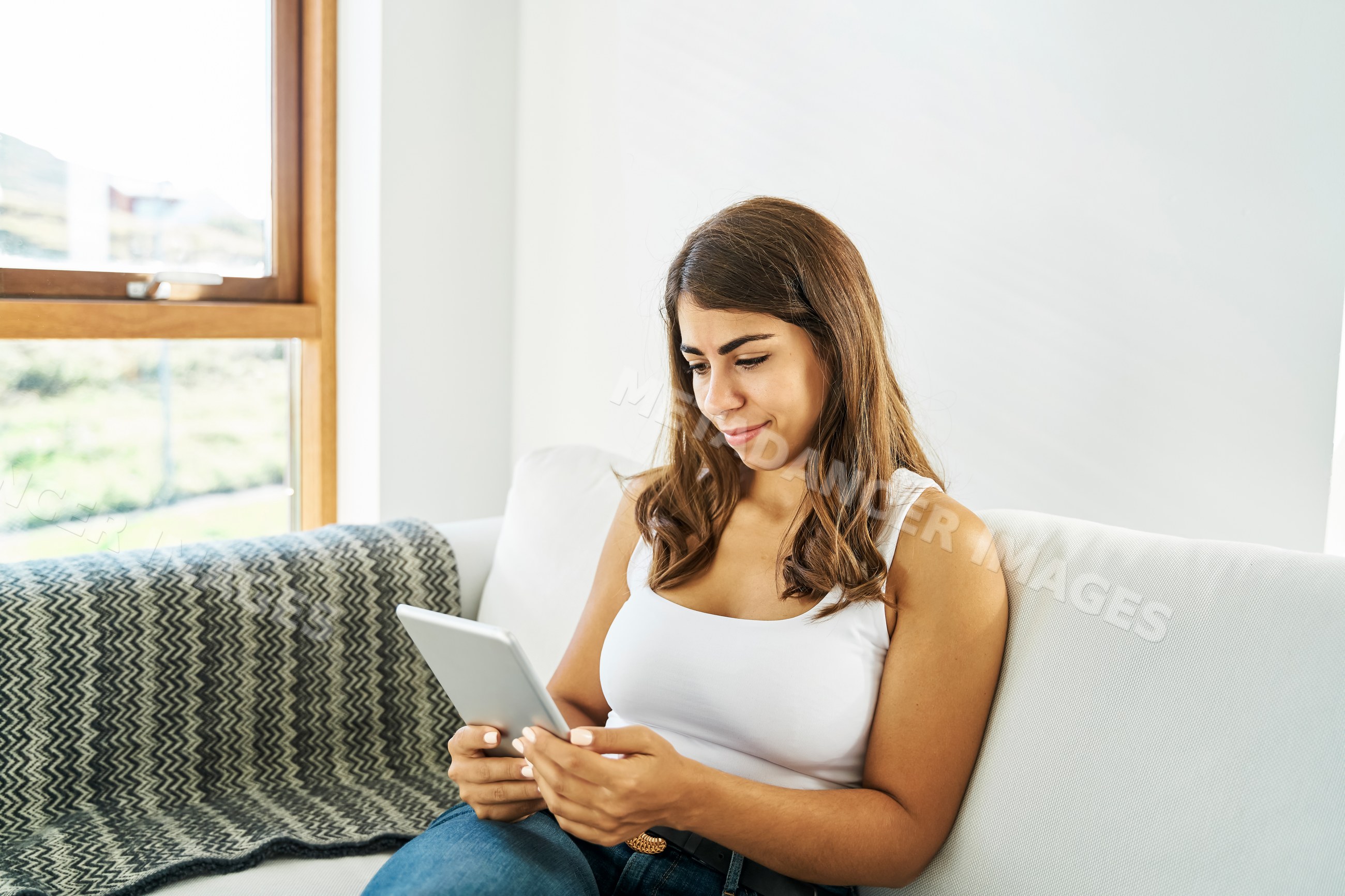 A white woman sitting on a sofa and using a tablet