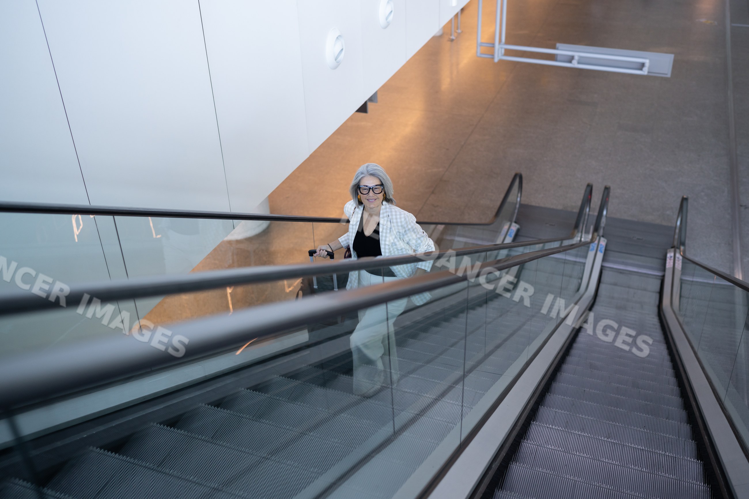 Businesswoman riding escalator carrying luggage inside modern building