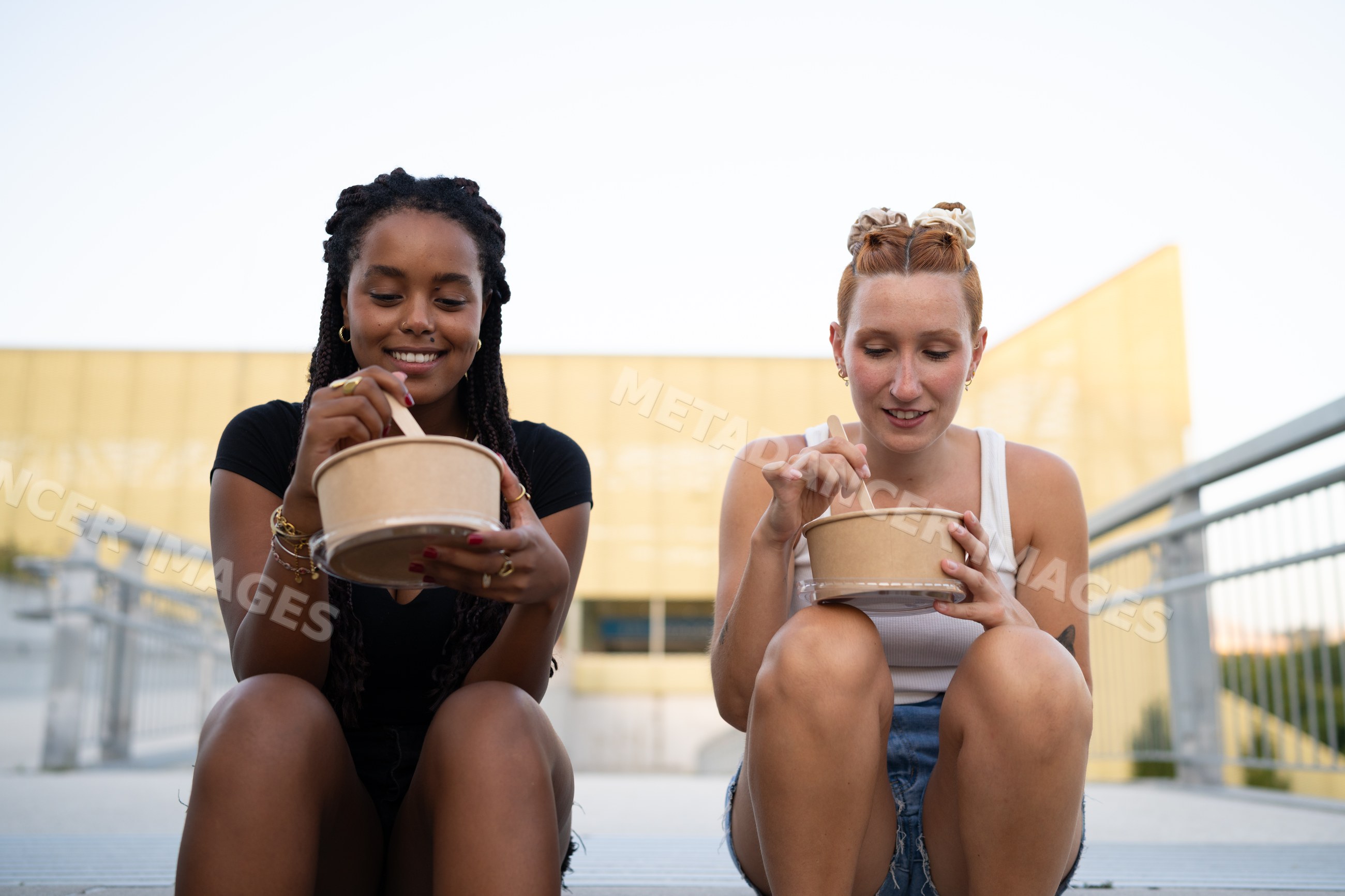 Two white and African American women eating casual meals sitting