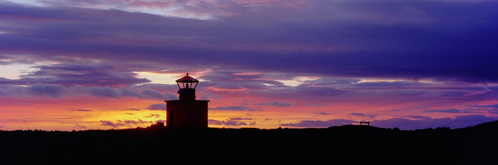Lighthouse silhouette at colorful sunset over coastal horizon