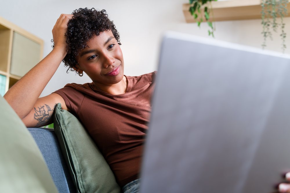 African American woman using laptop sitting on couch with green pillow