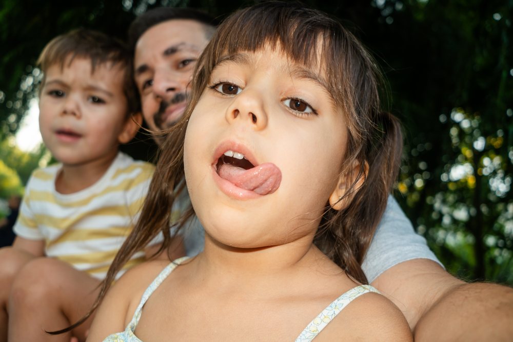 Young white girl sticks out tongue playfully with family outdoors
