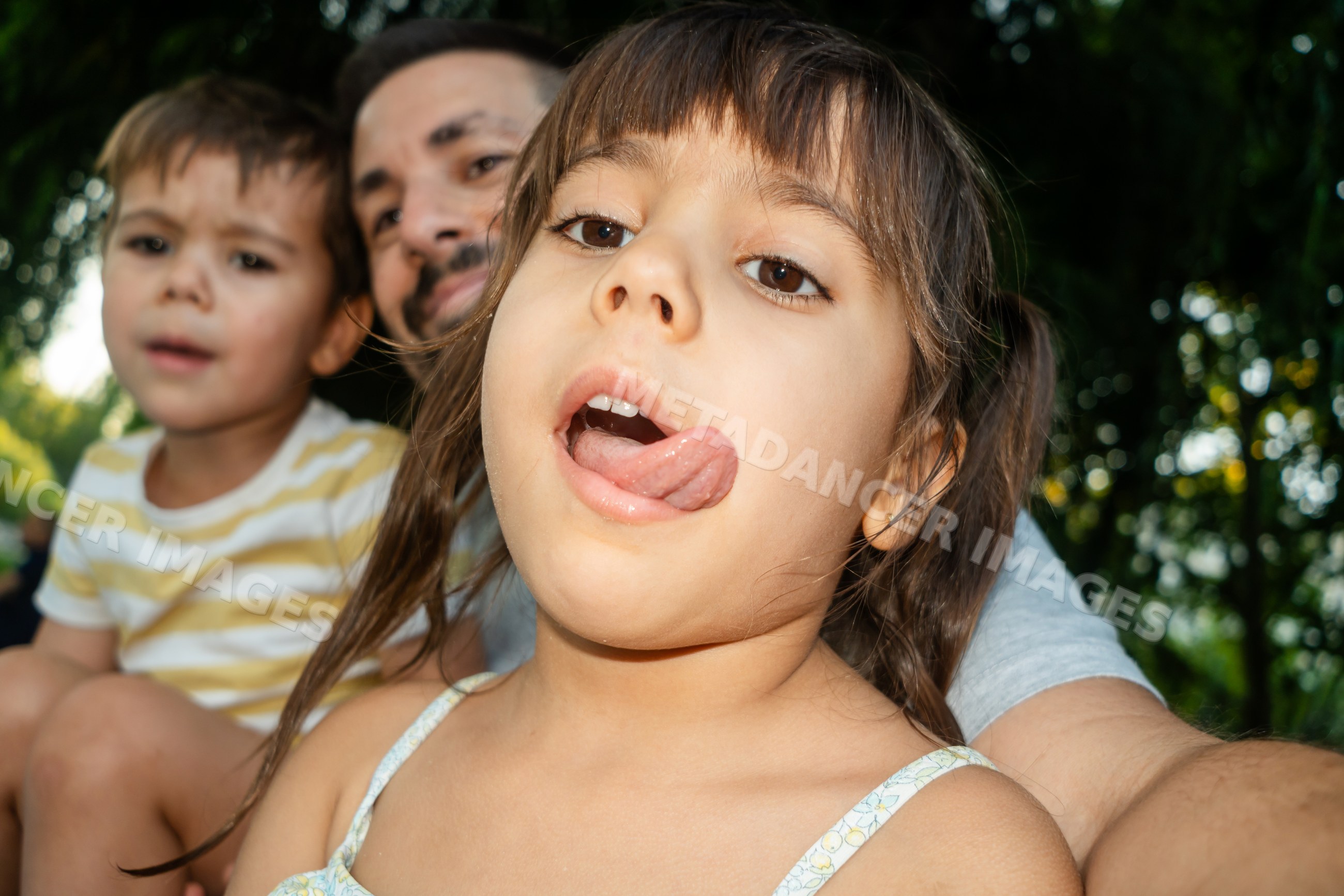 Young white girl sticks out tongue playfully with family outdoors