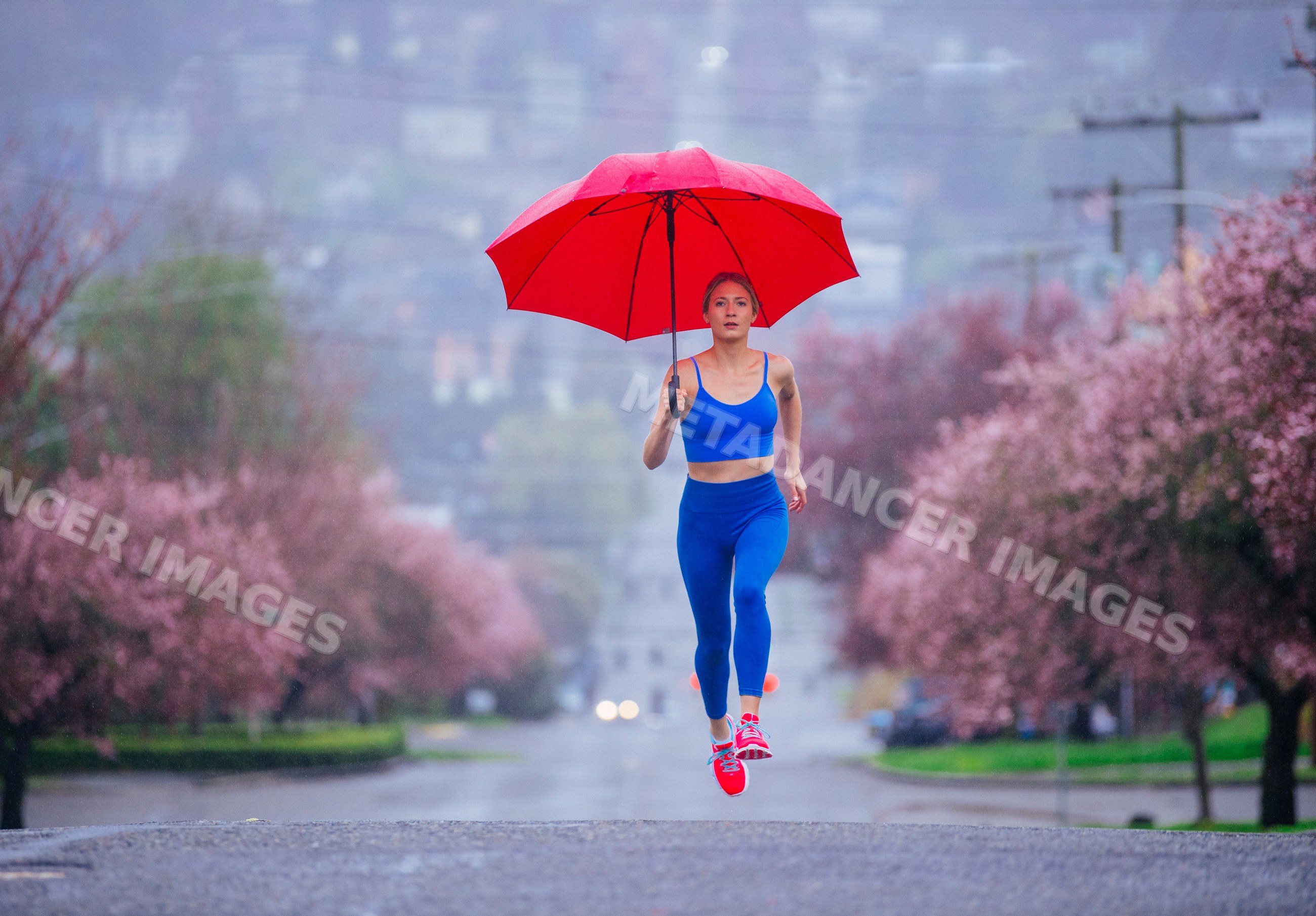 White woman running with red umbrella on street in spring rain