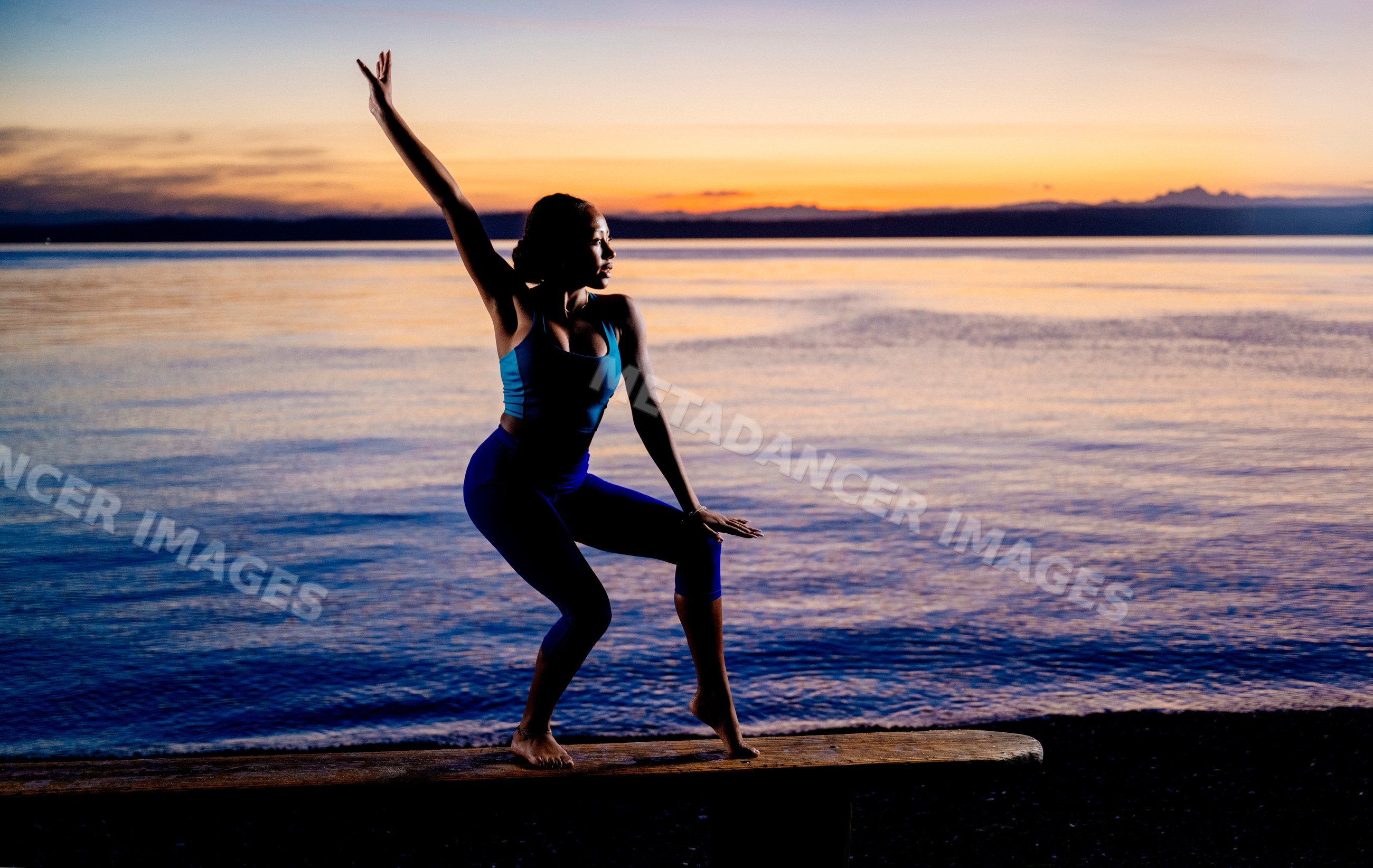 Hispanic woman balancing on wooden bench by ocean at sunset in the USA