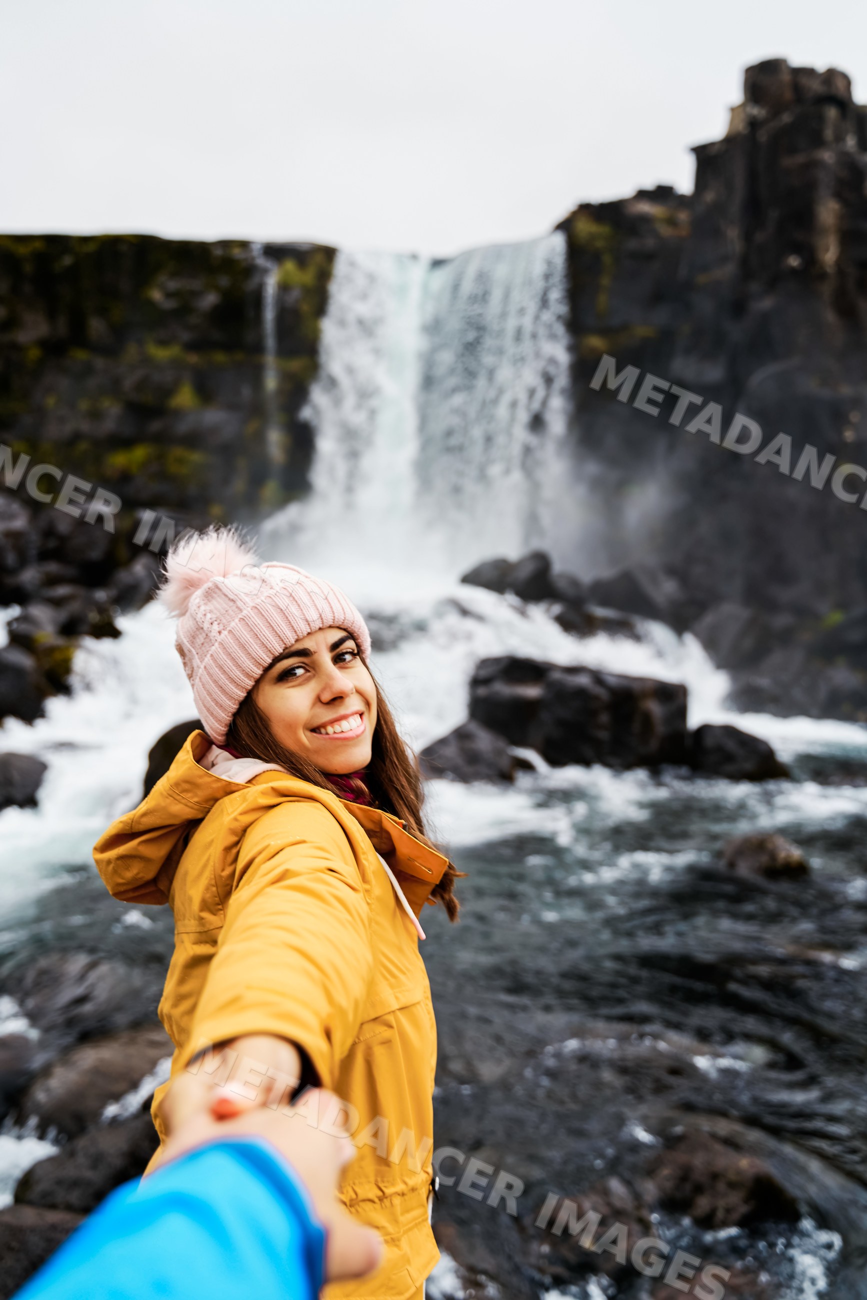 A white woman smiles holding hand near a waterfall in Iceland