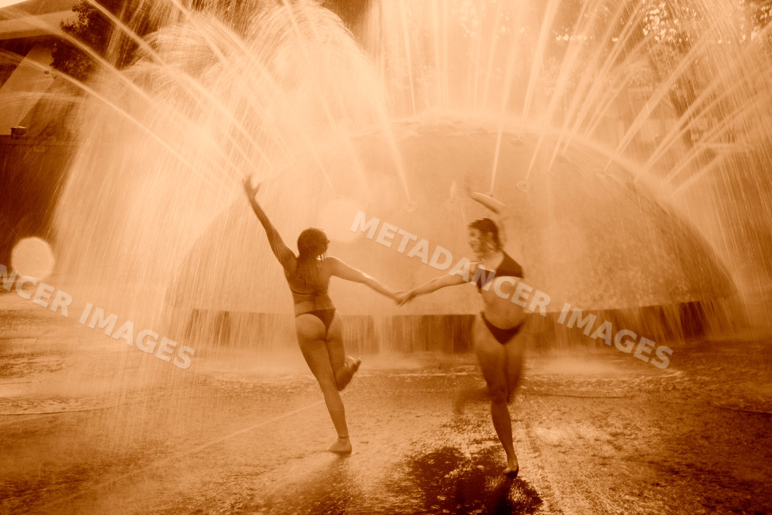 Two white women dancing and practicing acrobatics under fountain water