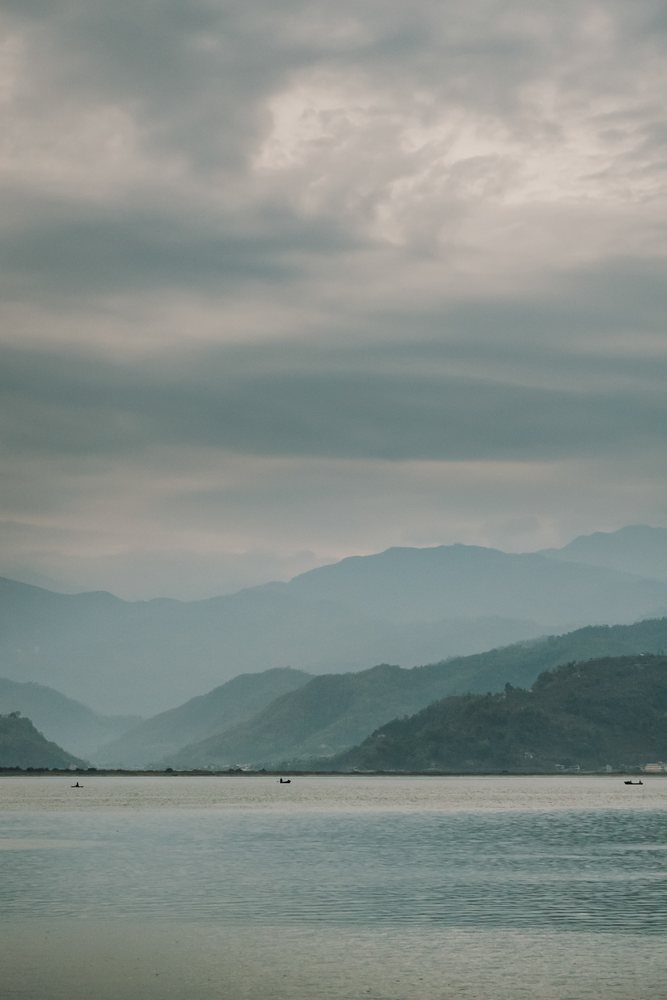 Calm lake with boats and mountainous landscape under cloudy sky