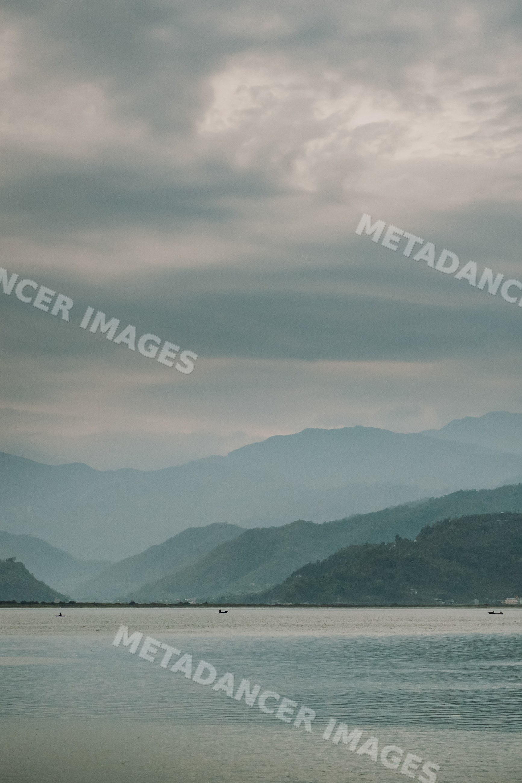 Calm lake with boats and mountainous landscape under cloudy sky
