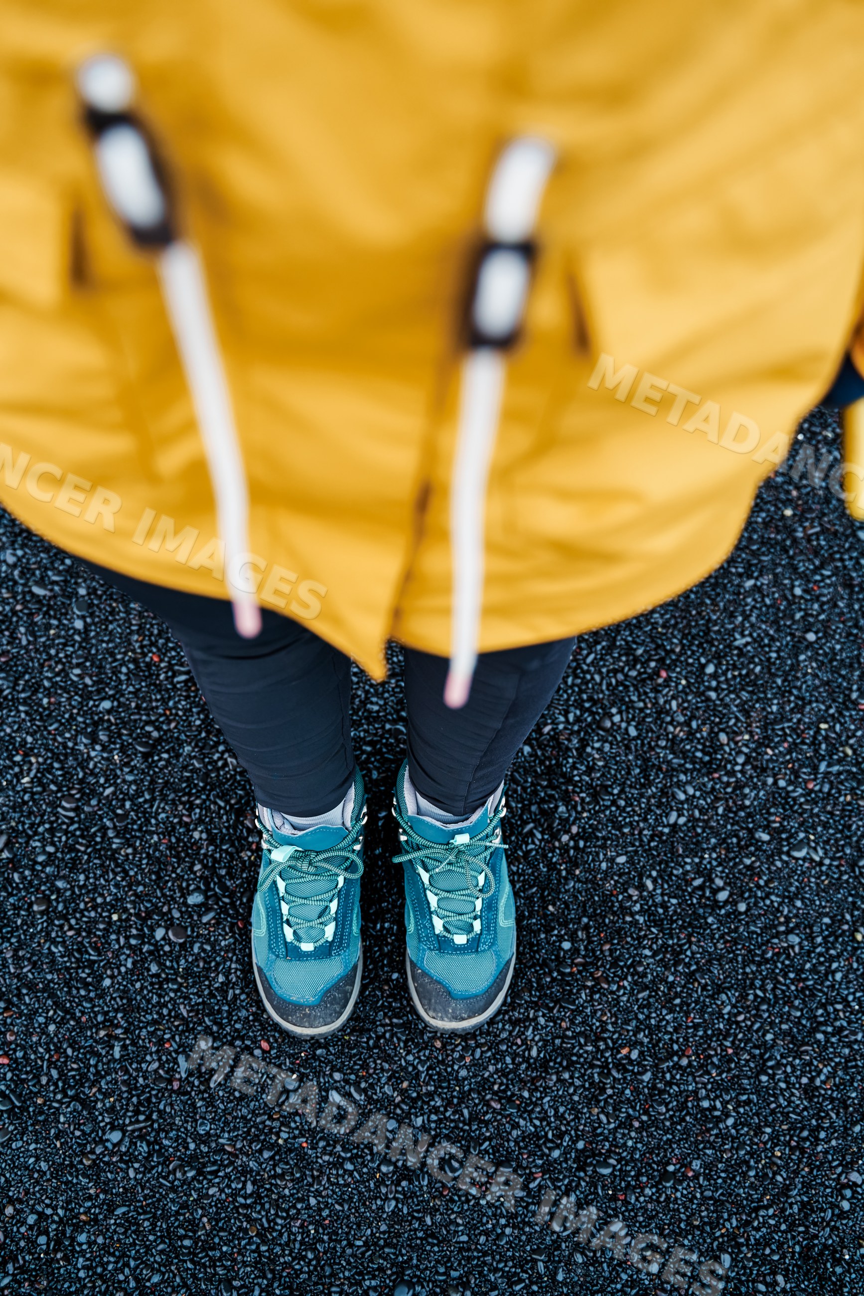 A white person wearing hiking boots stands on black pebbles