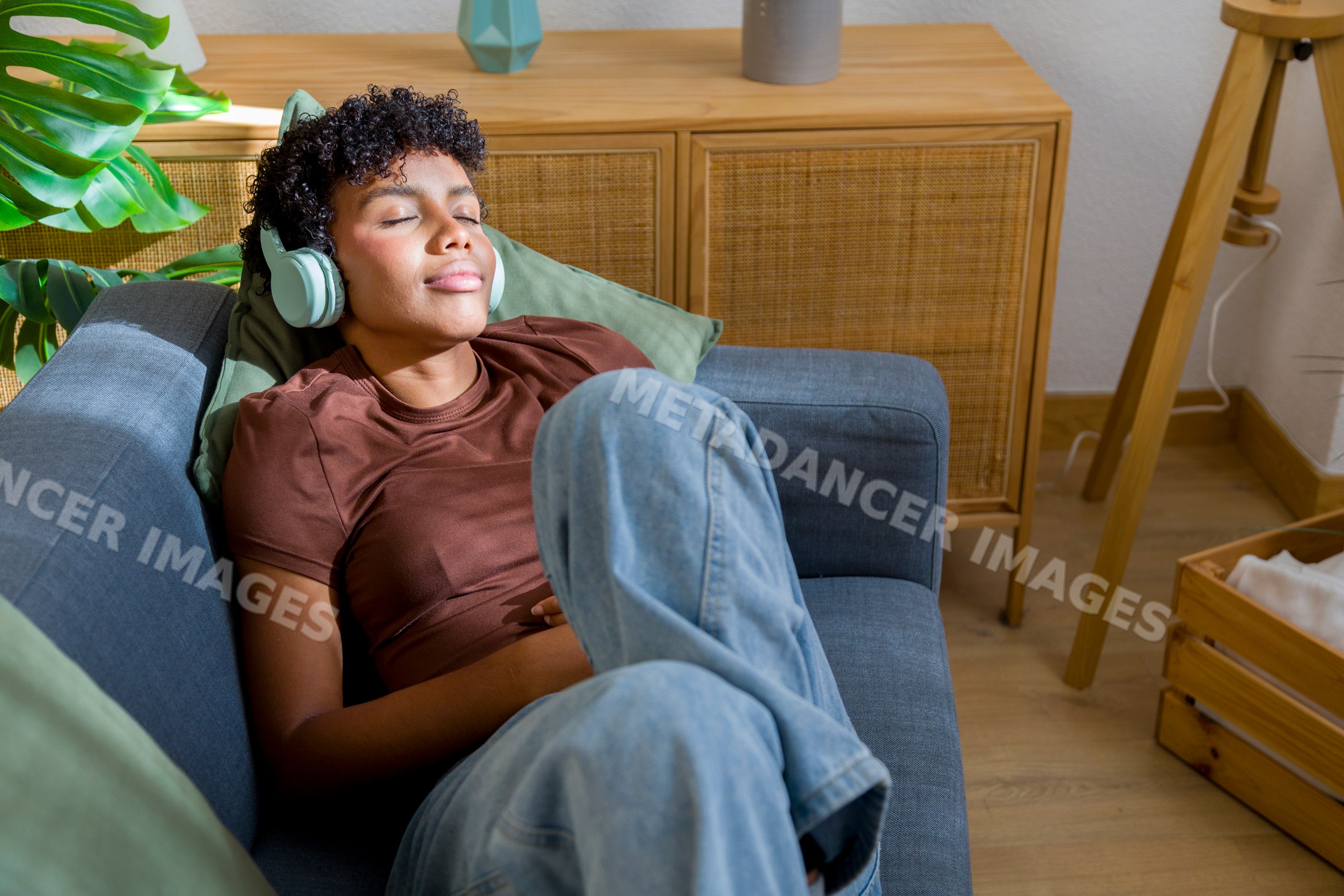 African American woman relaxing on sofa listening to music at home