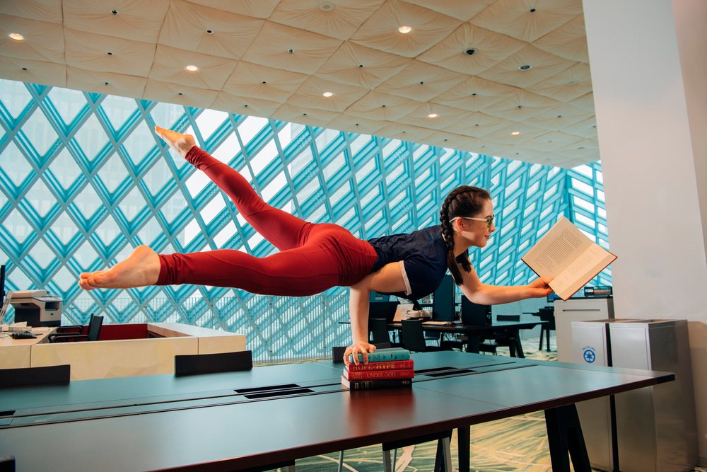 A woman performs a yoga handstand while reading a book