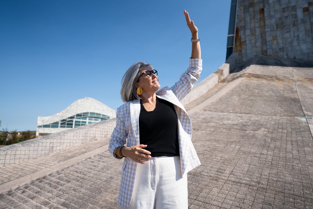 White woman raising hand outdoors by modern architecture