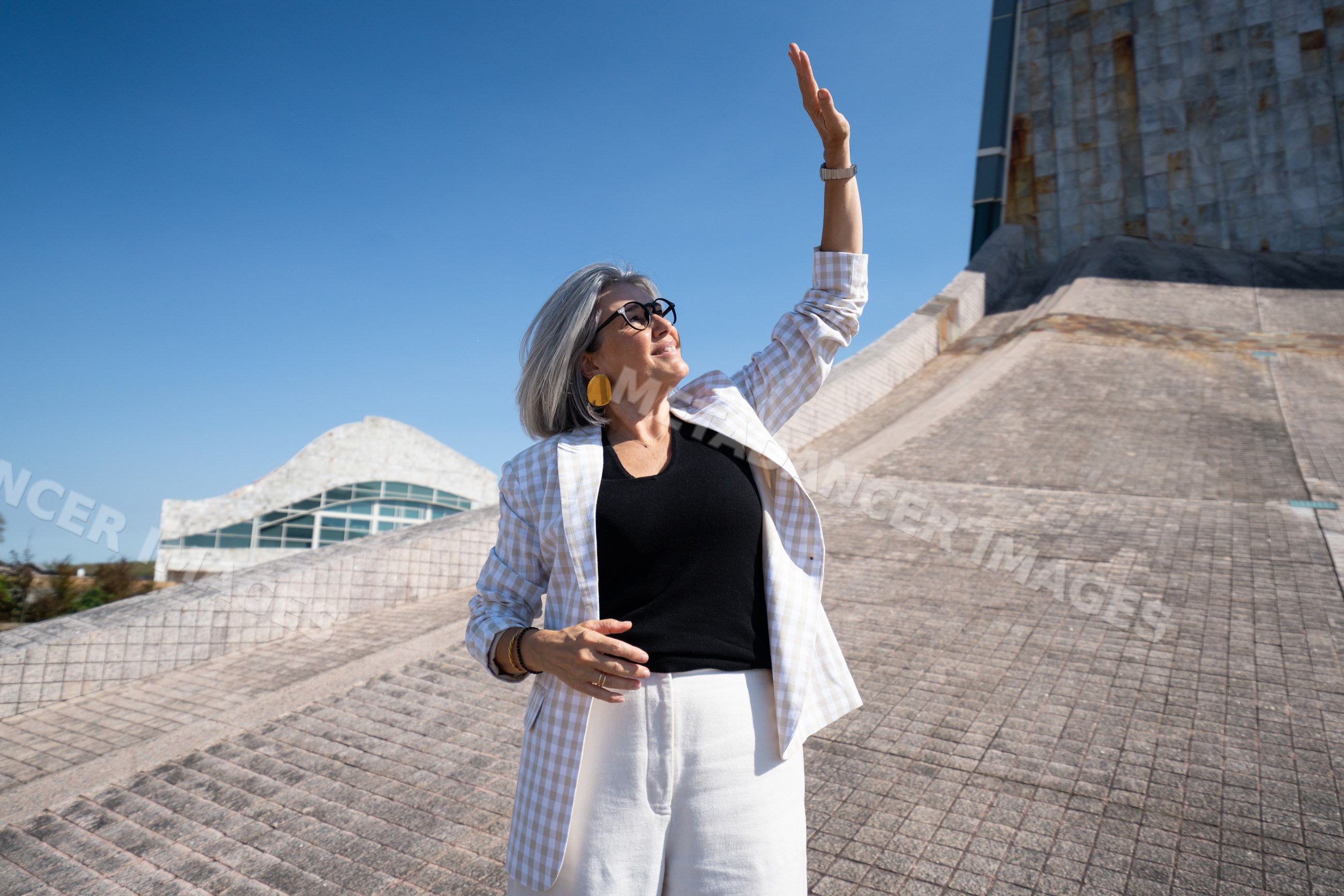 White woman raising hand outdoors by modern architecture