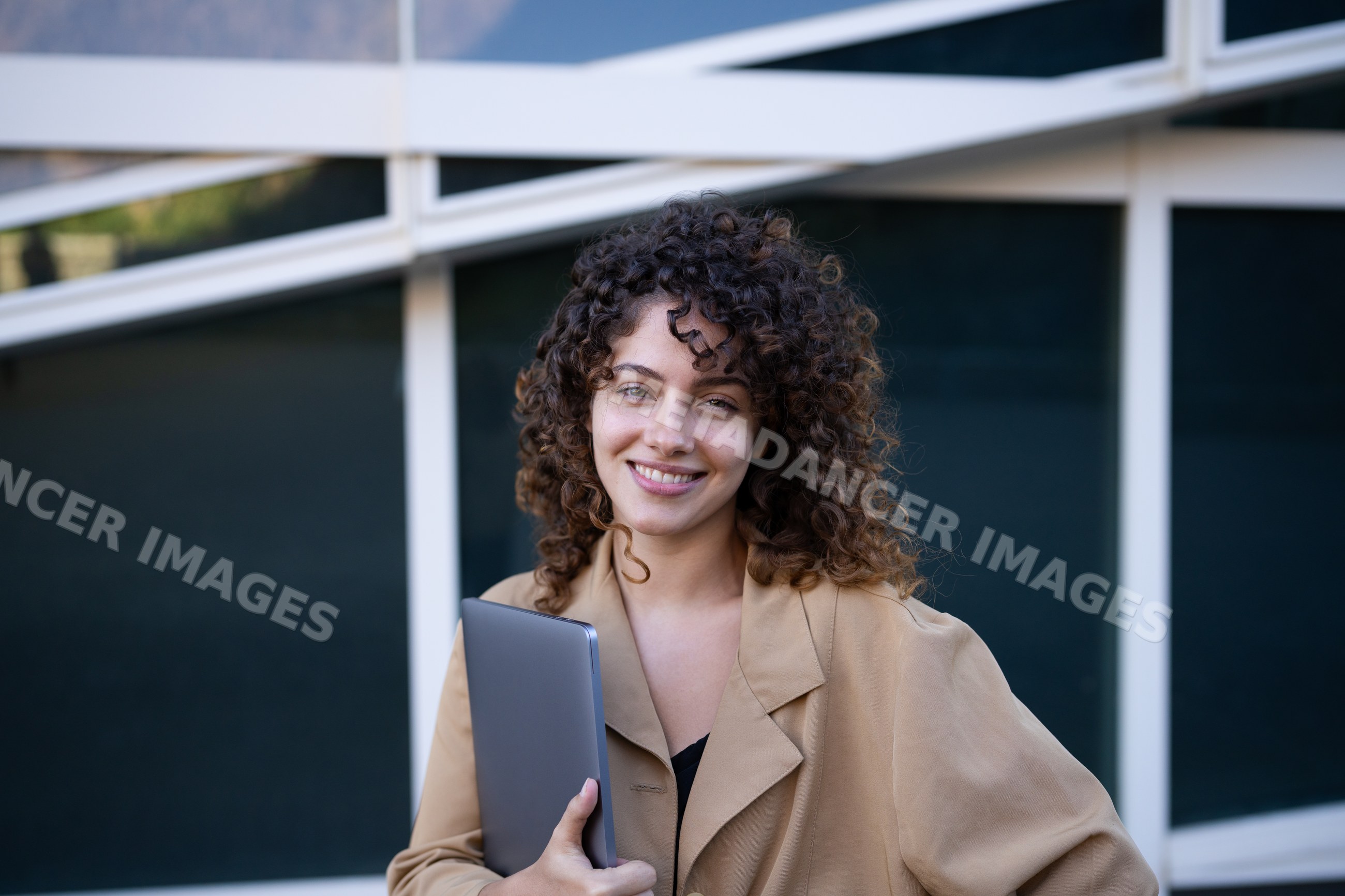 White woman with curly hair holding laptop outdoors