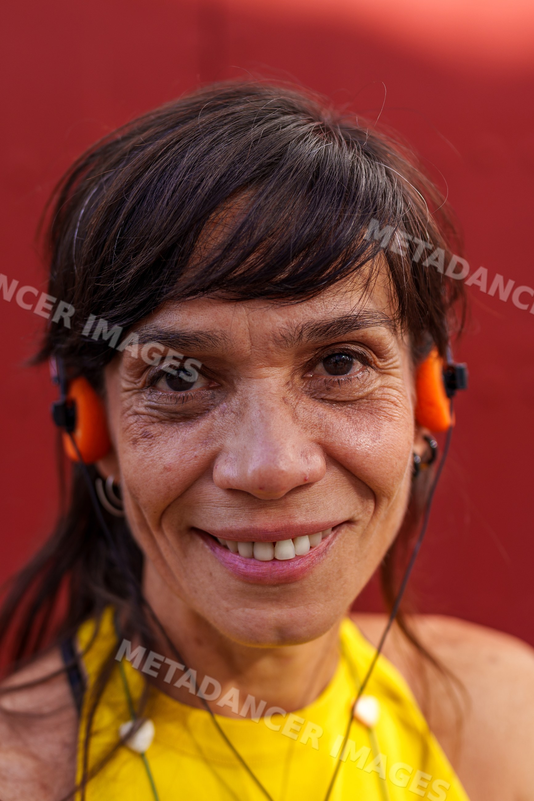 Hispanic woman smiling with orange headphones against a red background