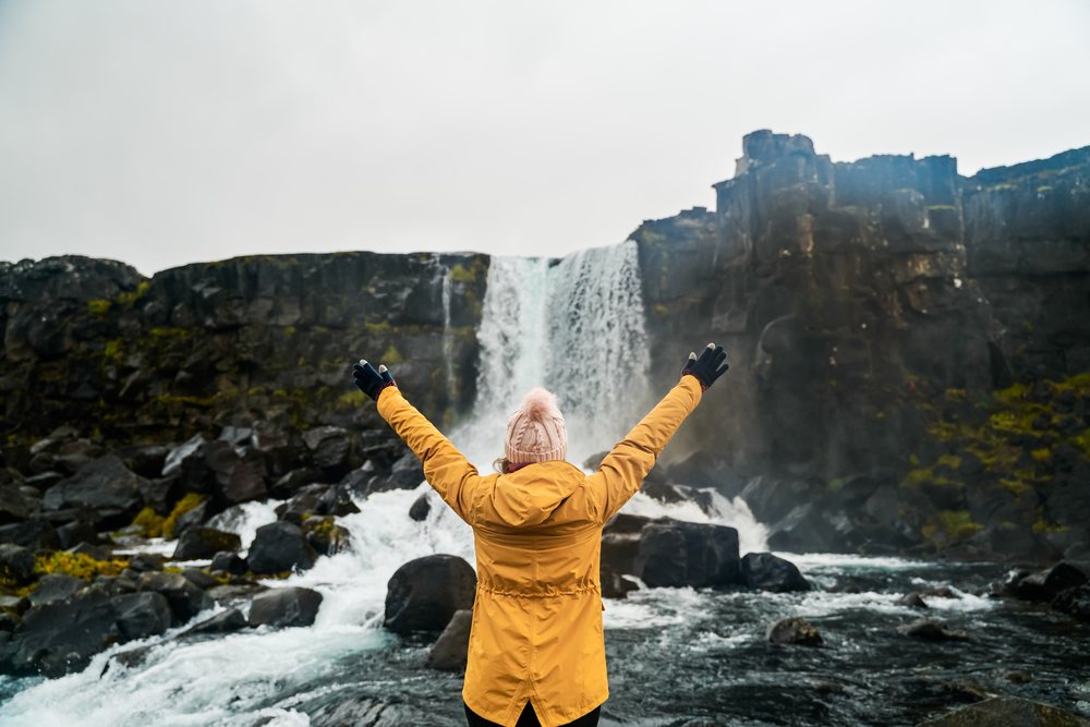 A white woman in a yellow jacket enjoys a waterfall in Iceland's