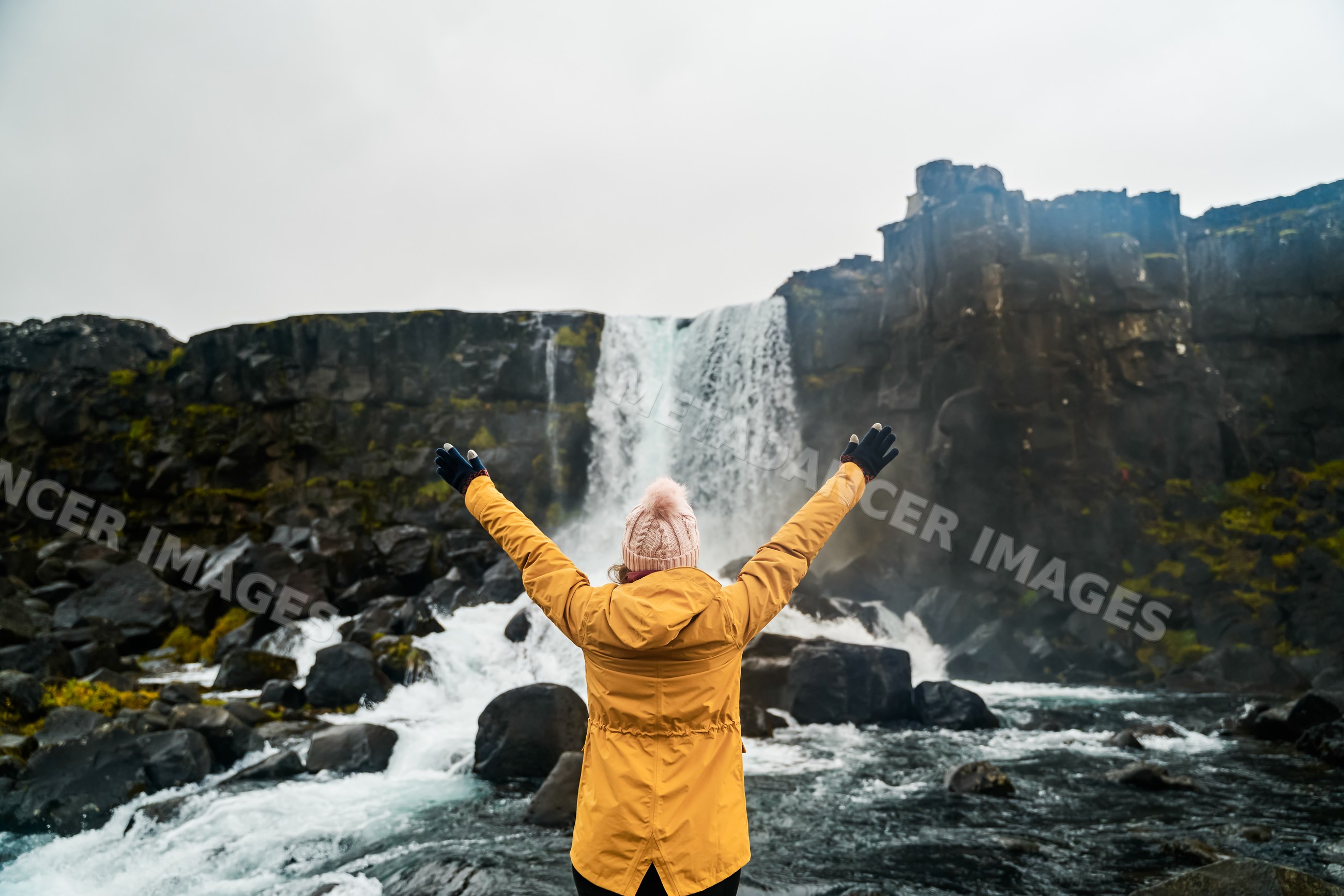 A white woman in a yellow jacket enjoys a waterfall in Iceland's