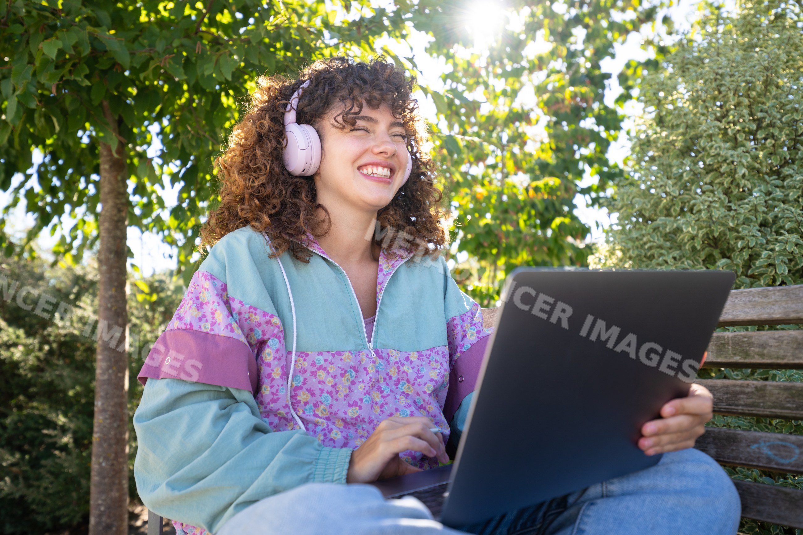 White woman using laptop with headphones outdoors on a sunny day