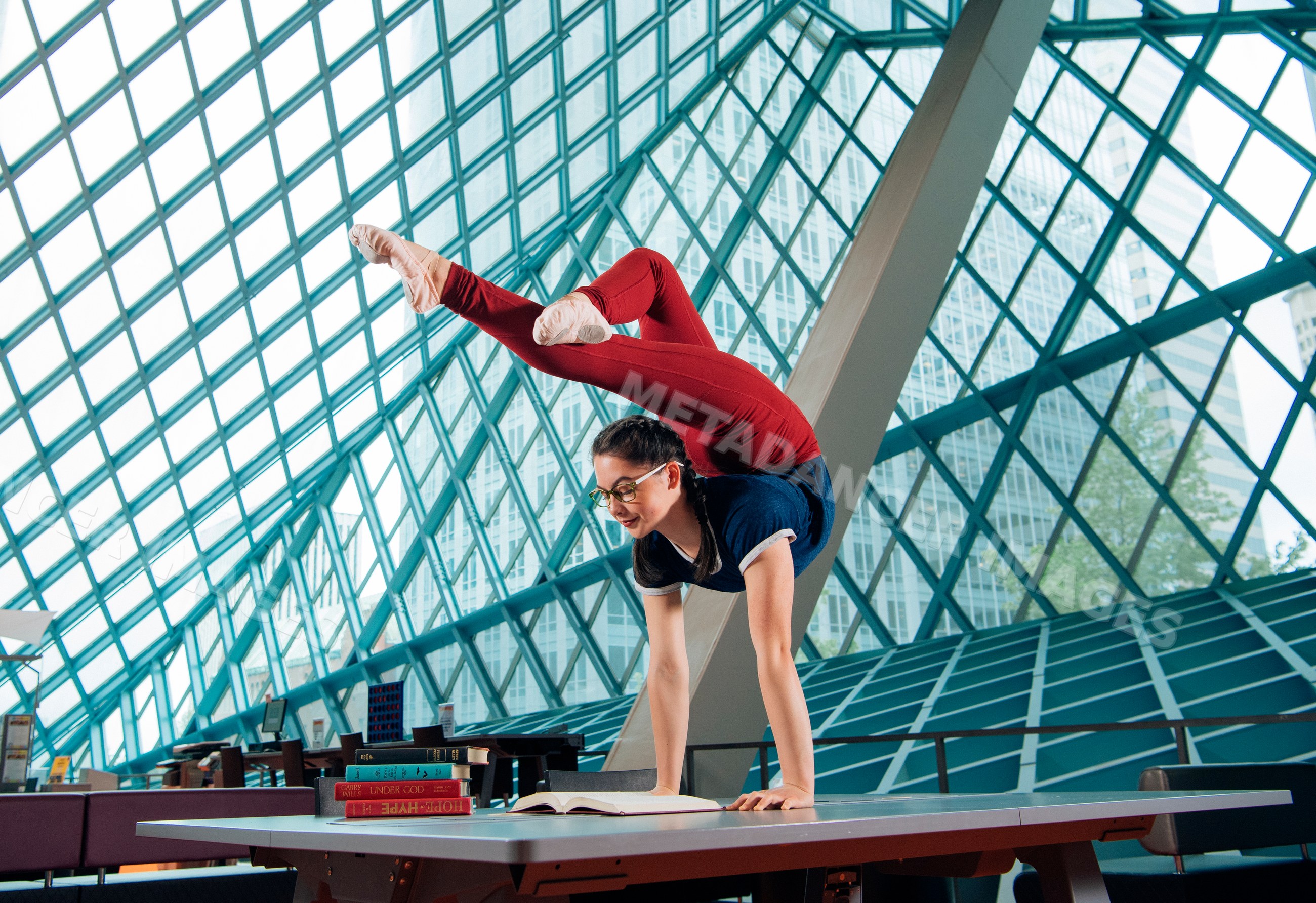 A young woman practices a handstand yoga pose on a table in a library