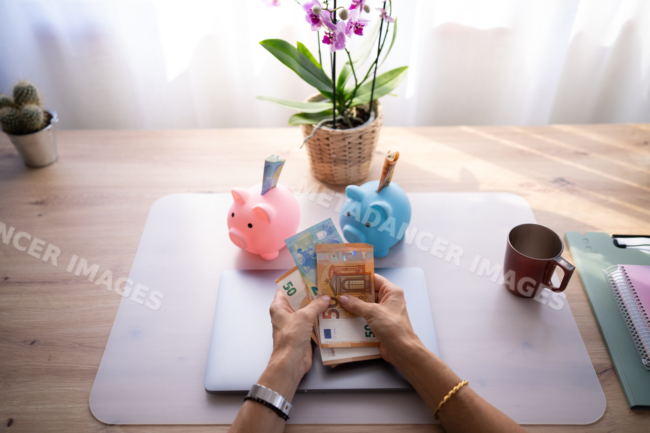 Hands counting euro banknotes with piggy banks on a wooden table