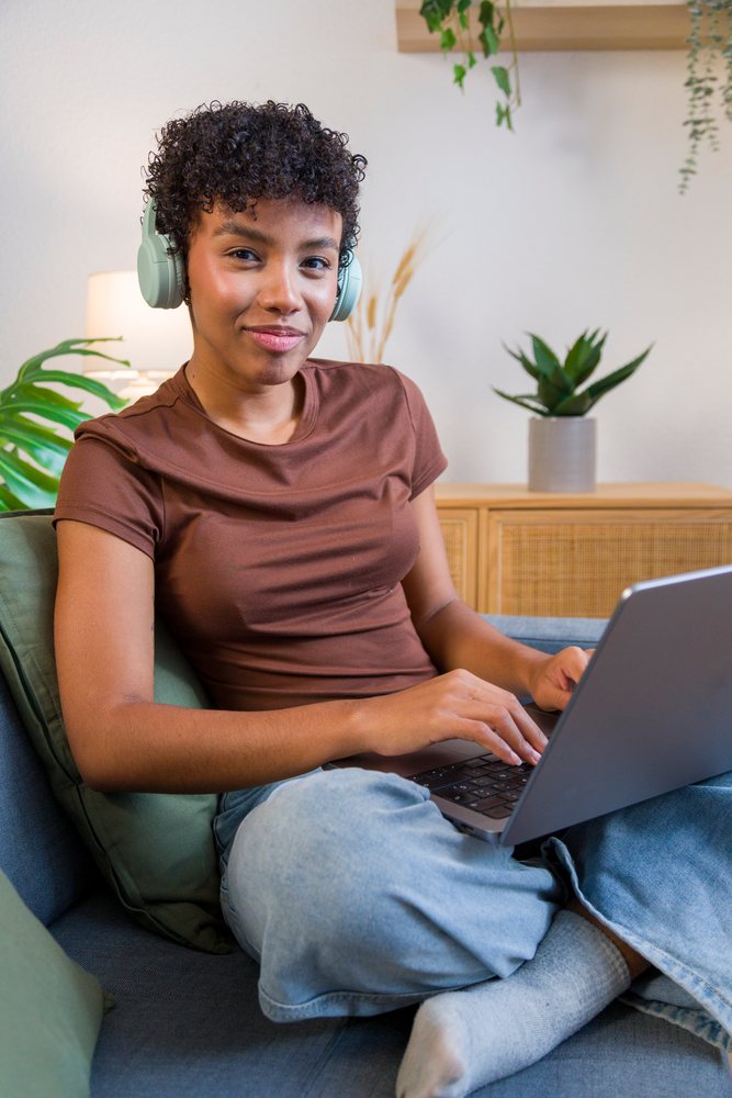 Young African American woman typing on laptop seated on sofa wearing