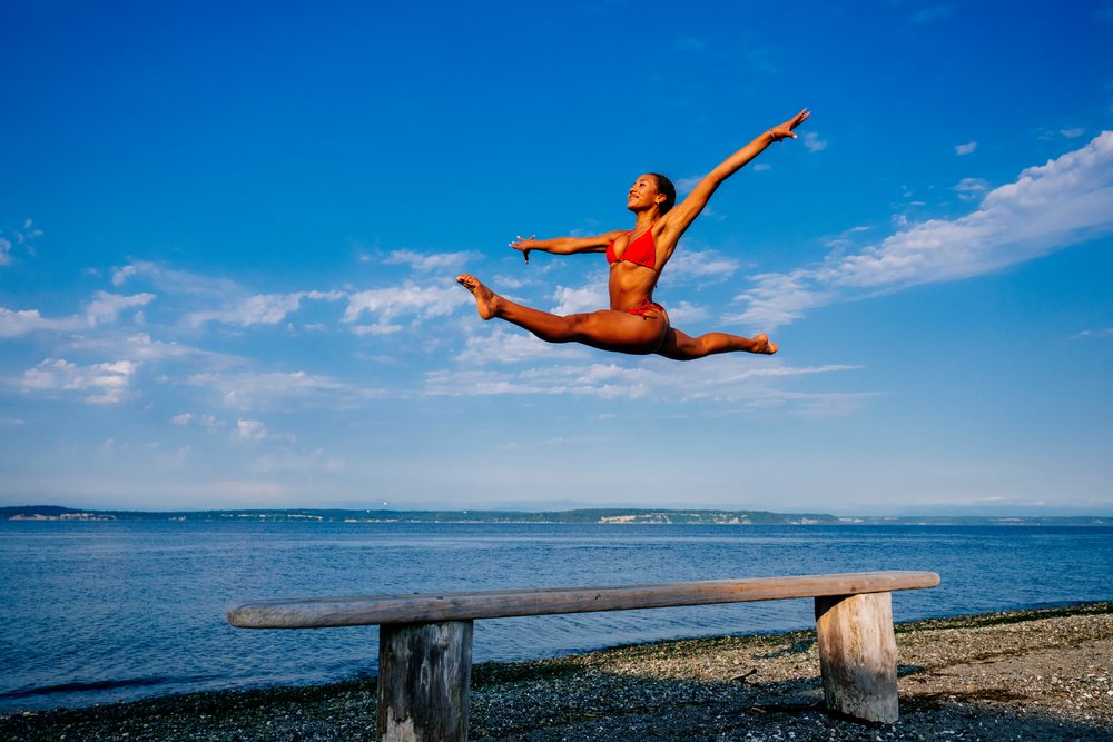 A woman leaps in a split over a beam on a beach in WA, USA