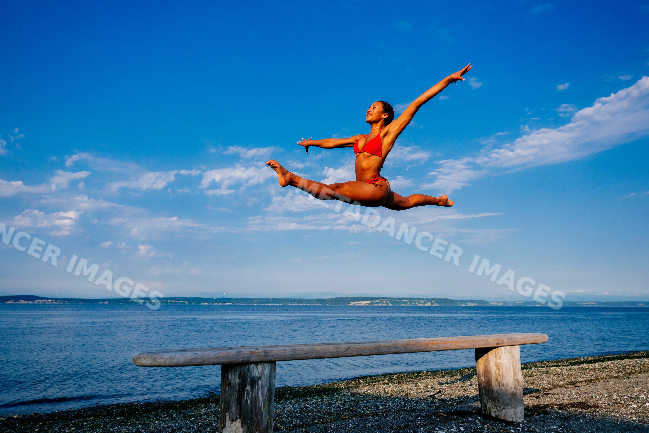 A woman leaps in a split over a beam on a beach in WA, USA