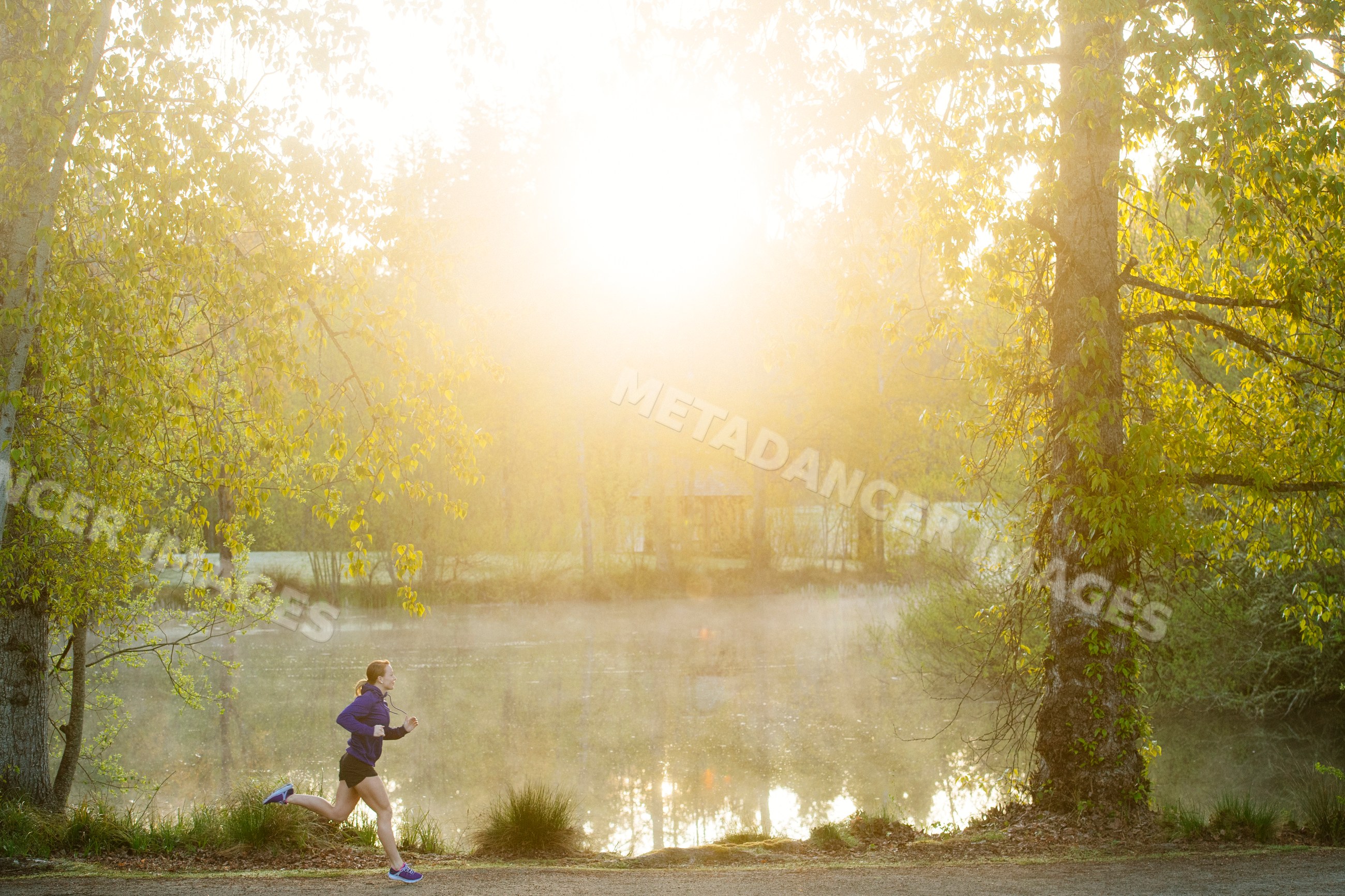 White runner jogging along trail through park in morning mist