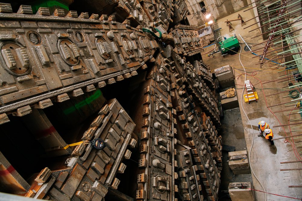 White construction workers inspect a large tunnel boring machine