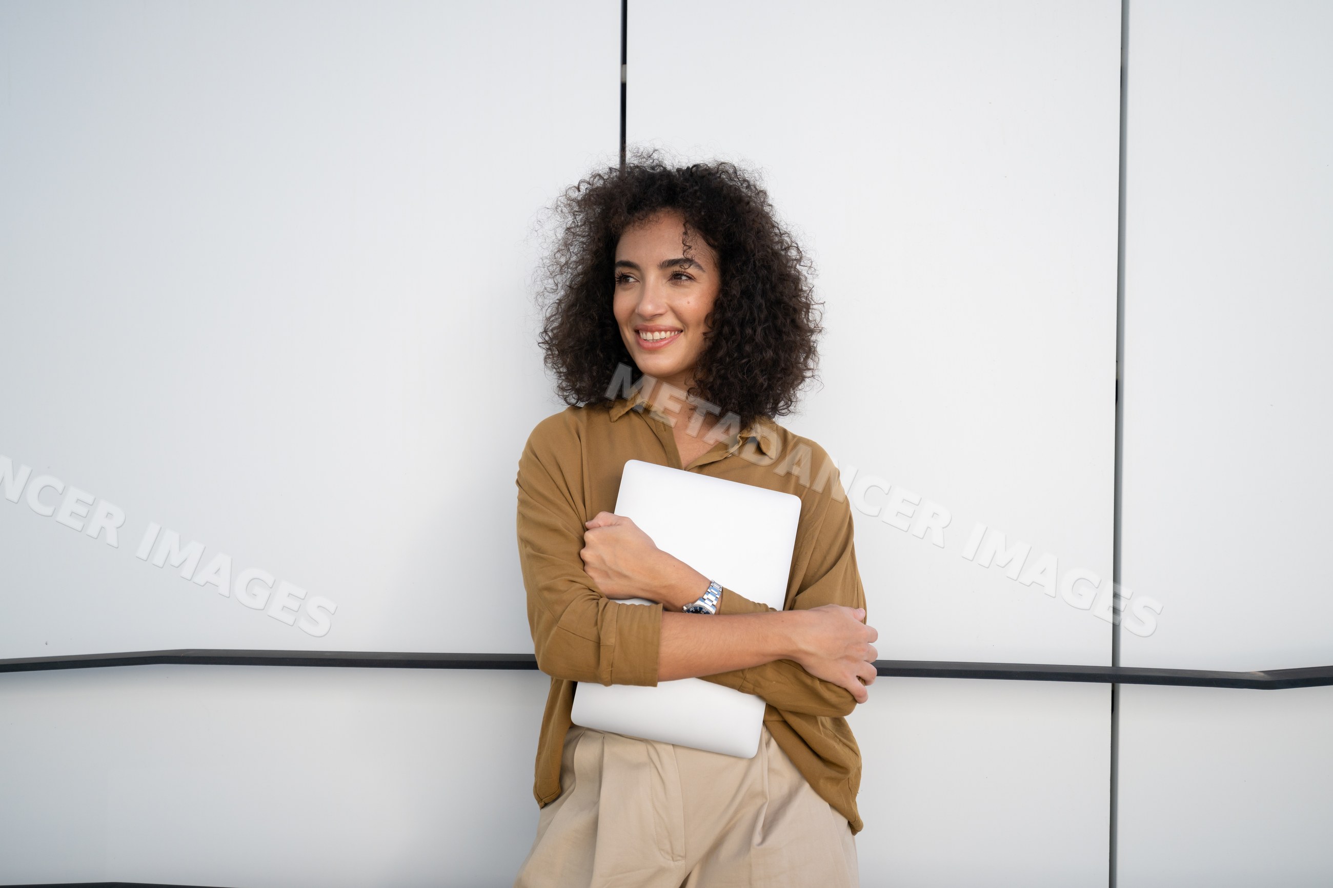 Woman holding laptop and smiling against white wall in Madrid, Spain