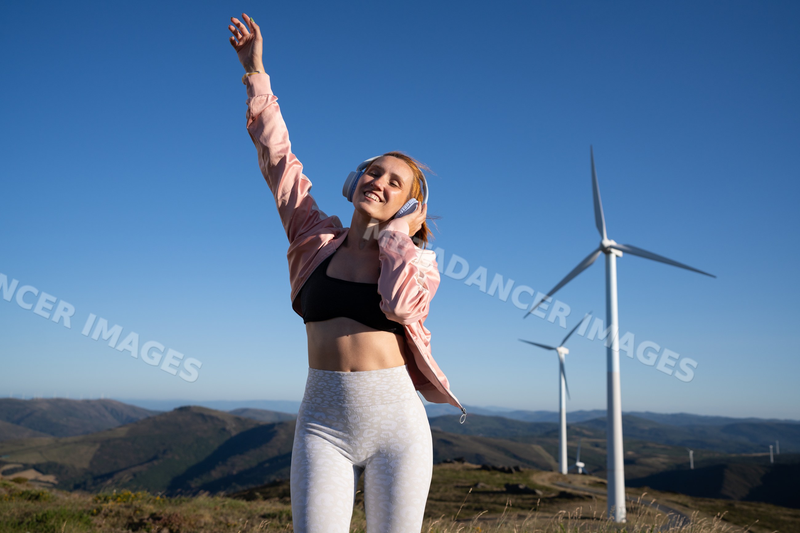 White woman enjoying music outdoors near wind turbines in Galicia