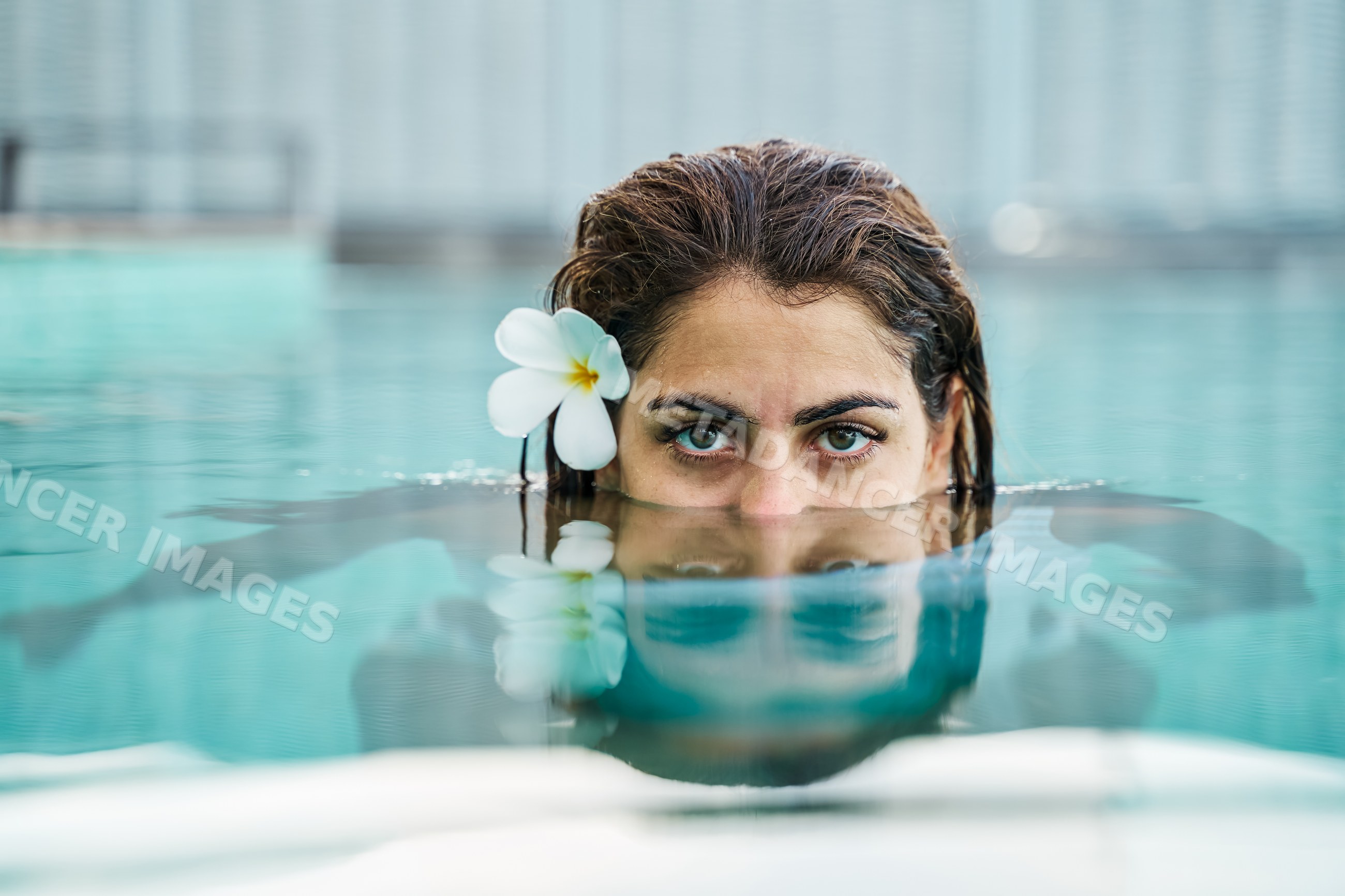 A white woman swims partially submerged in a calm blue pool