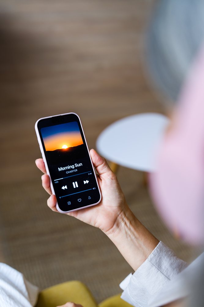 White person holding smartphone with music player paused on 'morning