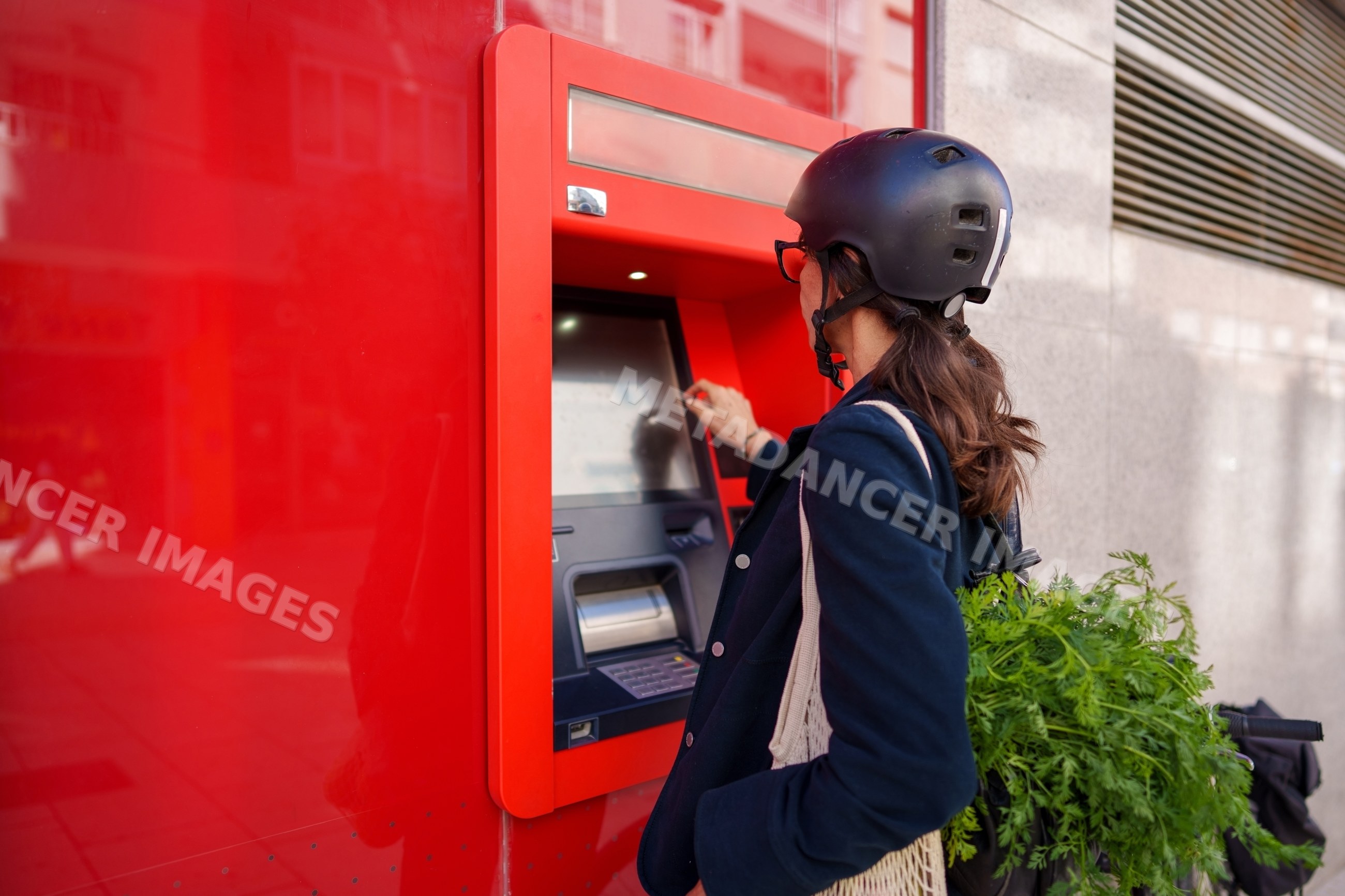 Hispanic woman using outdoor atm with bicycle and shopping greens
