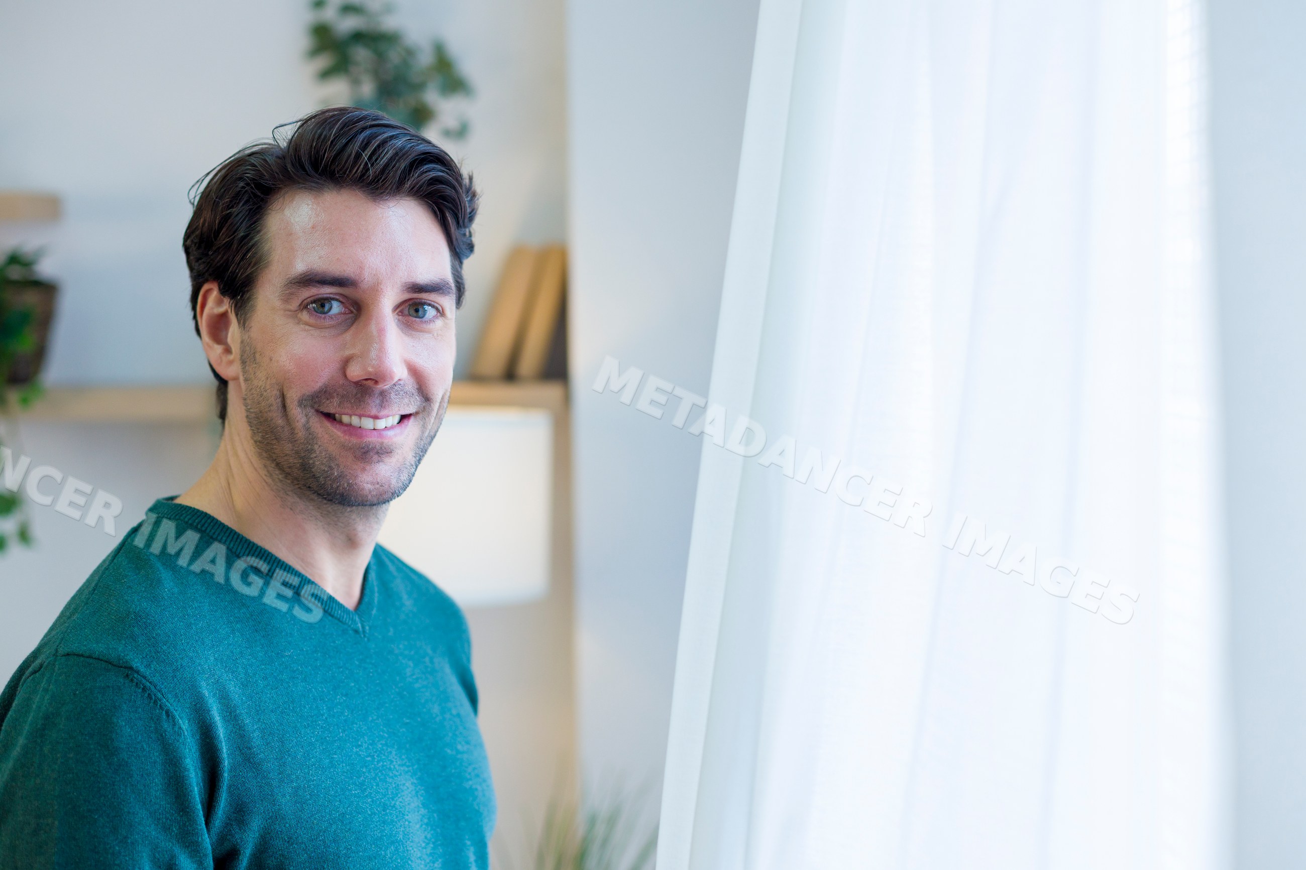 Man smiling indoors near window with white curtains in modern home