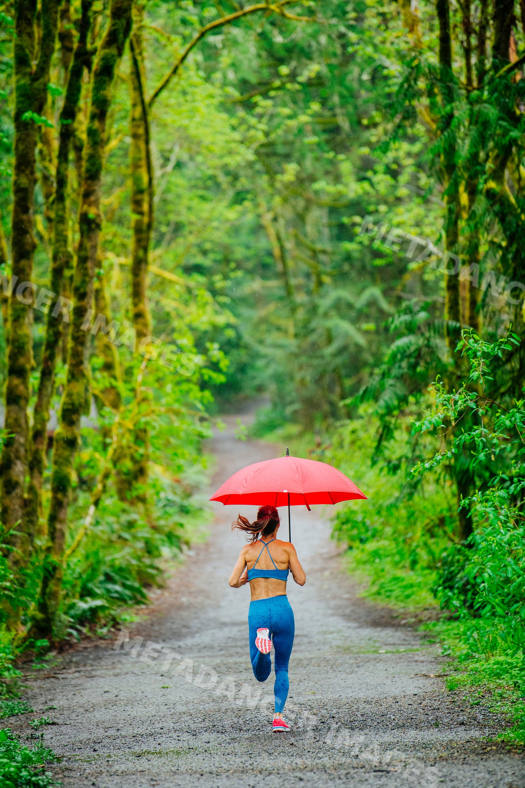 White woman running on forest path with red umbrella in rainy weather