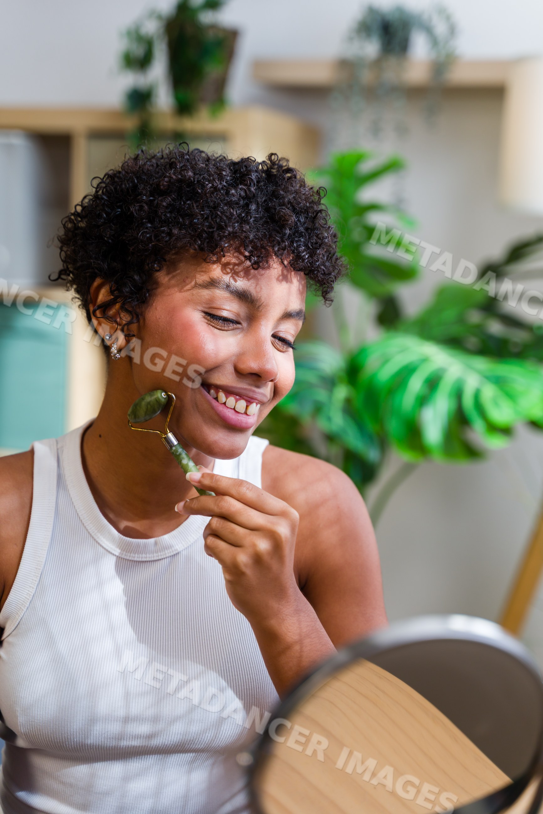 African American woman using jade face roller in bright room