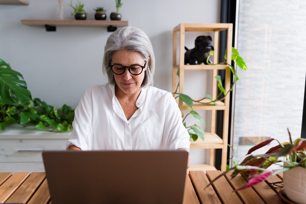 Senior white woman working on laptop at home office with plants