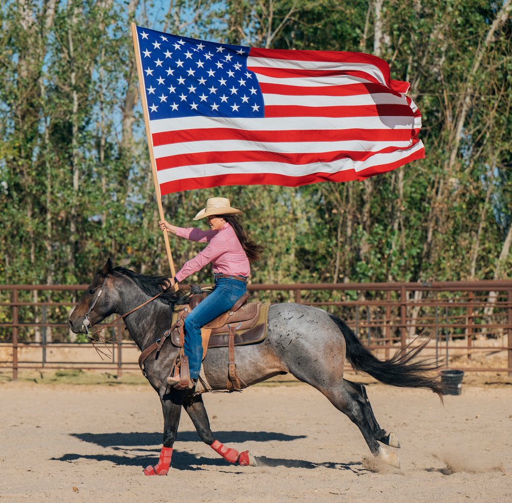 White woman galloping horse in arena holding american flag