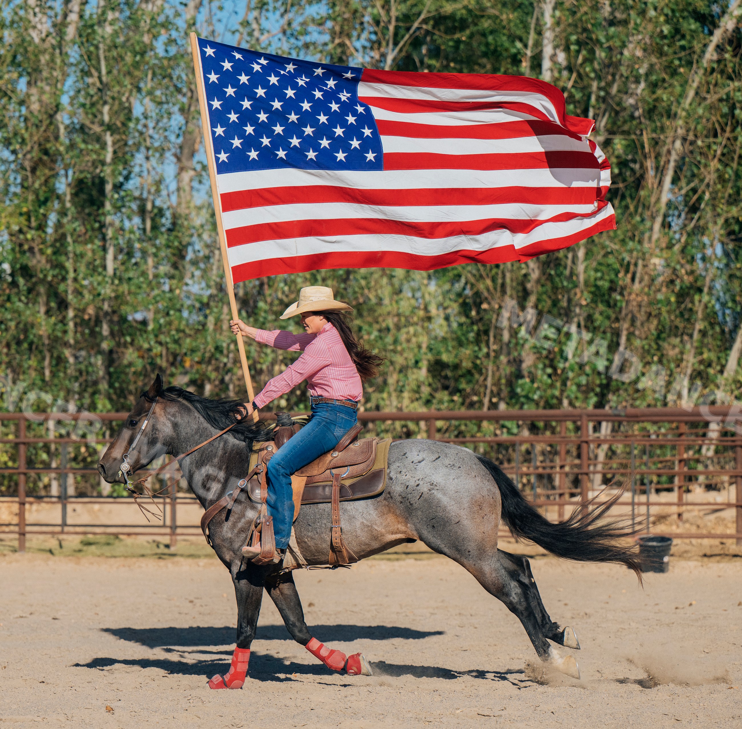 White woman galloping horse in arena holding american flag