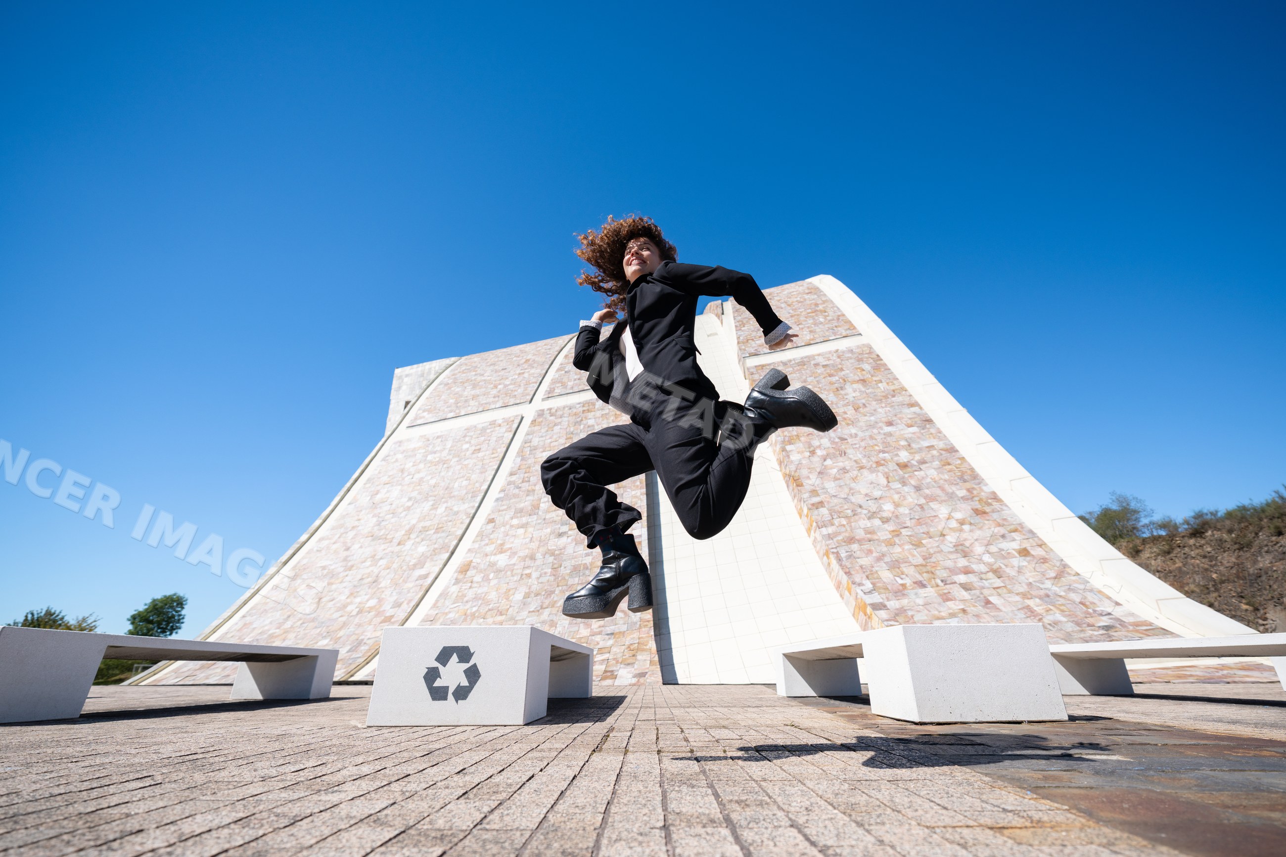 White professional woman jumping outdoors near modern building