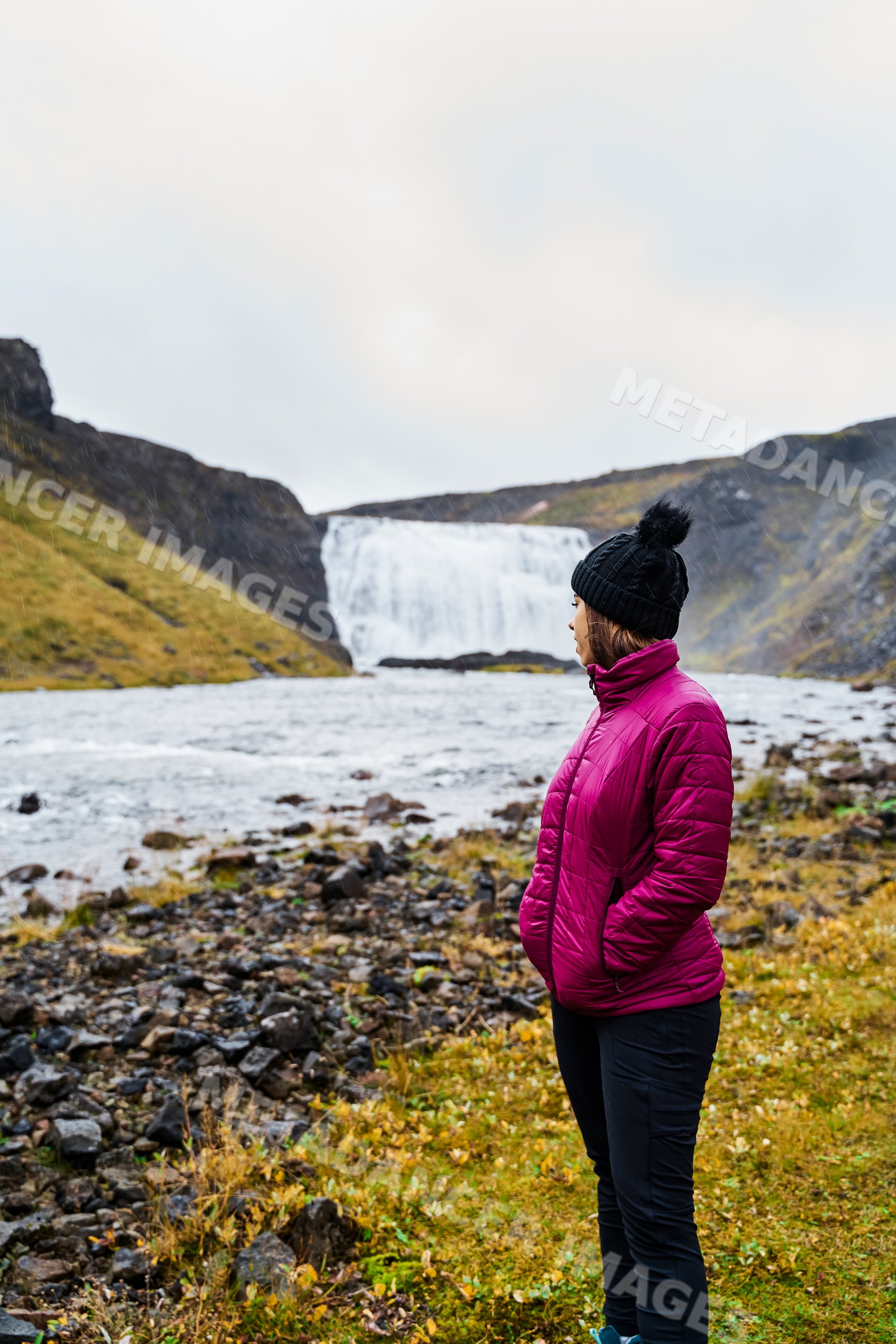 White Woman in winter clothes looking at a waterfall in Iceland