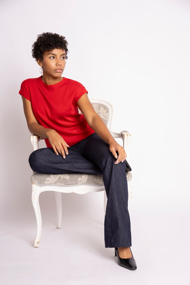 Hispanic woman sitting in chair wearing red shirt and dark jeans