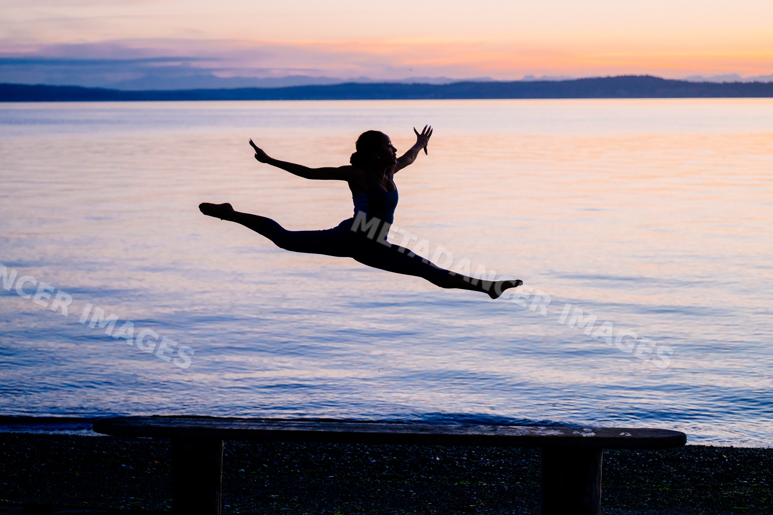 Hispanic woman performs split jump silhouette at sunset over lake