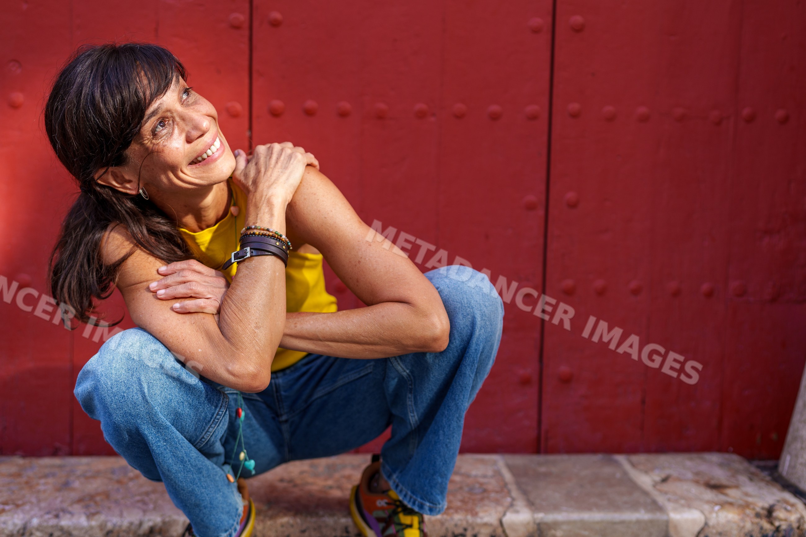 Hispanic woman smiling and squatting near red door outdoors in Málaga