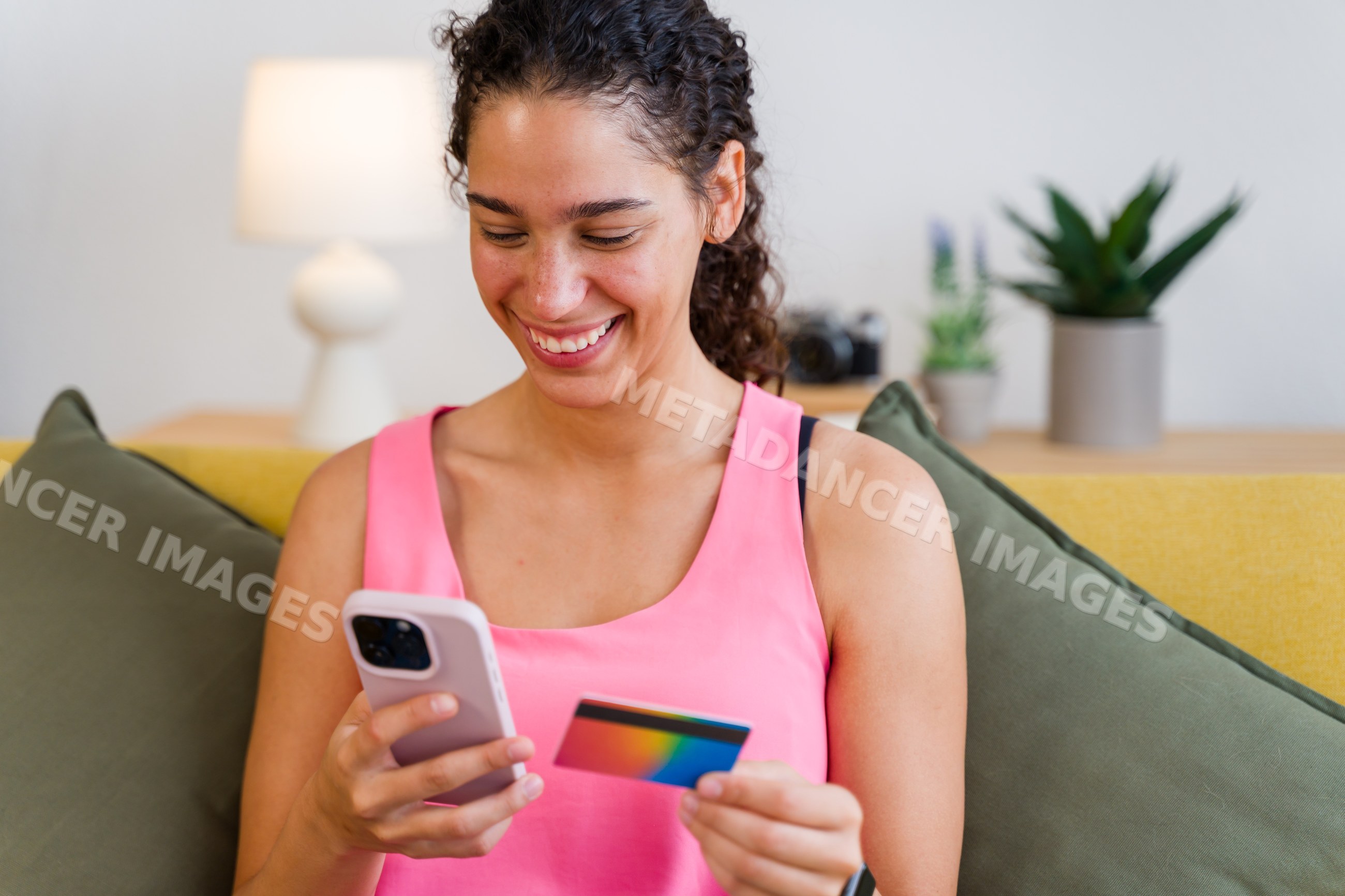 A Hispanic woman uses a smartphone and credit card for online payment